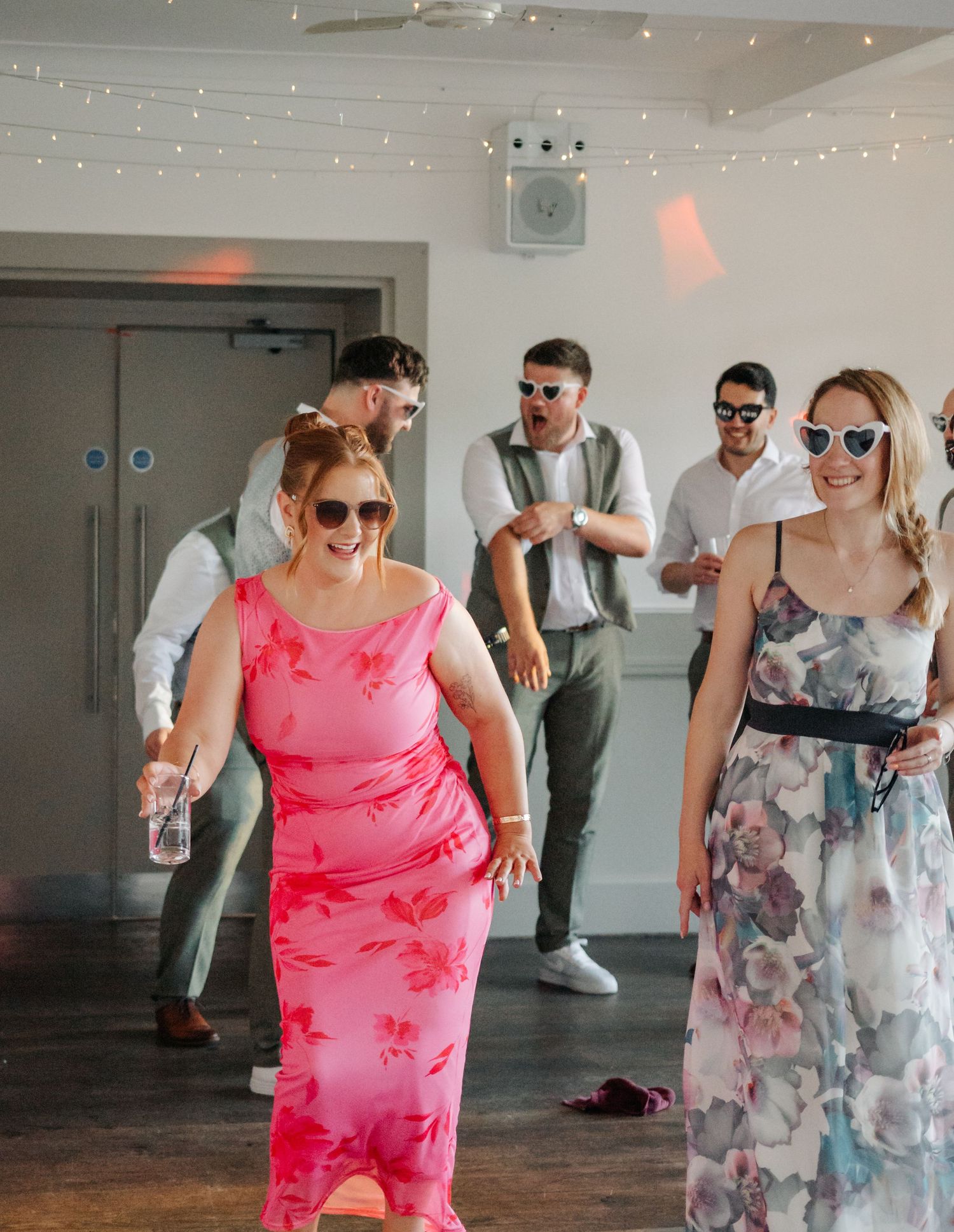 Party guests dancing and having fun at a celebration with string lights overhead in an indoor venue.