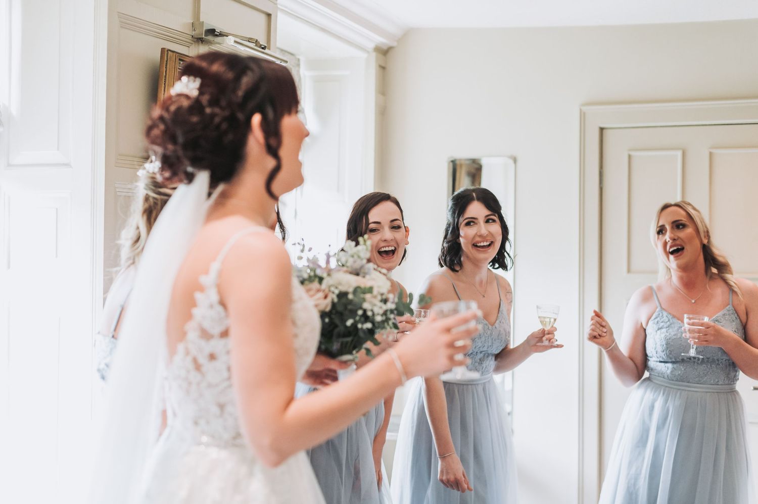 Bridal party getting ready in bright white room wearing elegant blue bridesmaid dresses.