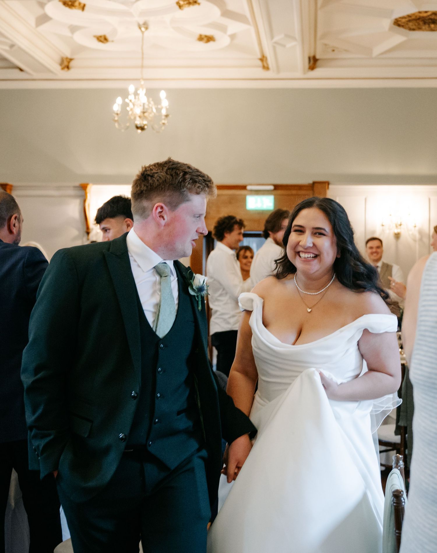 Wedding celebration in an elegant white room with ornate ceiling details and chandelier lighting.