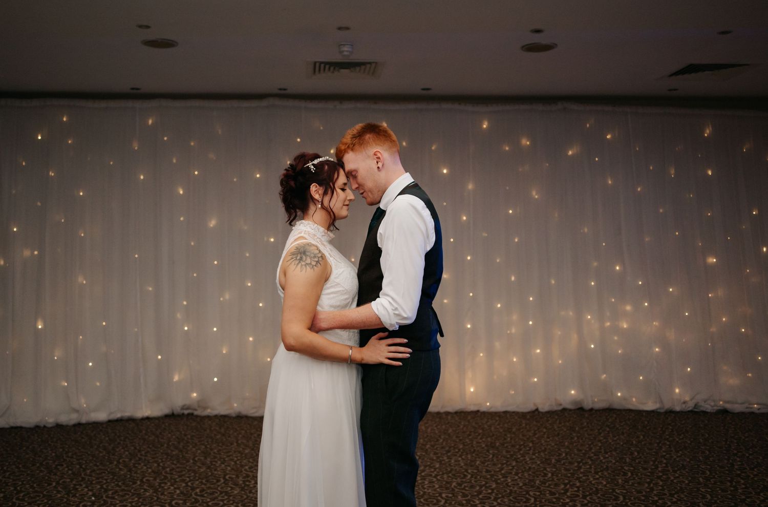 Couples dancing in a dimly lit reception hall with twinkling fairy lights in the background.
