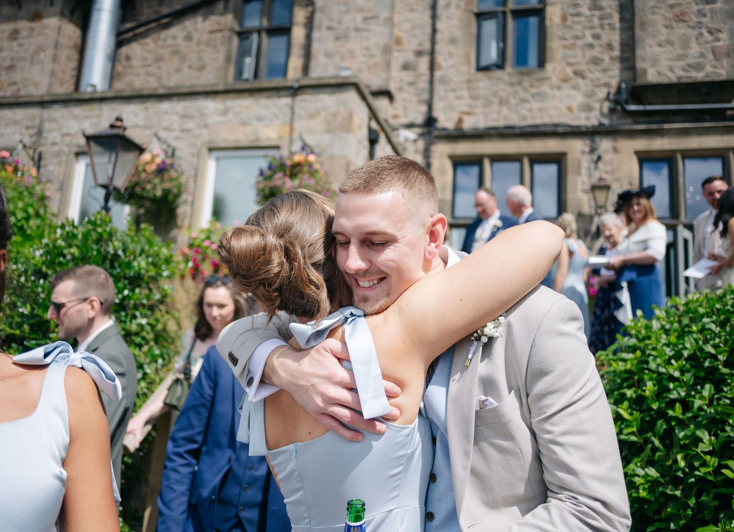 Wedding guests gather outdoors at a stone building venue during a celebration.