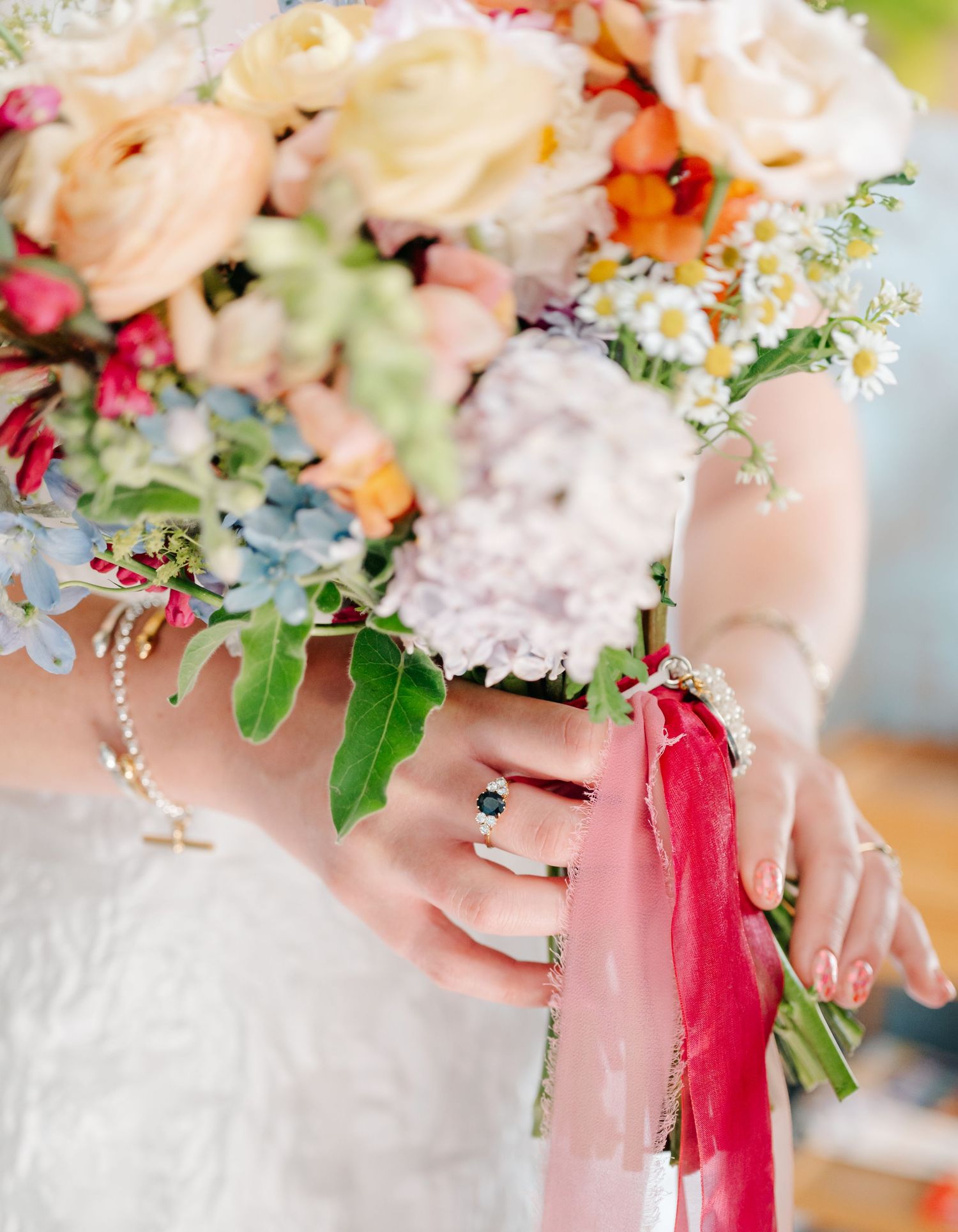 A close-up of hands holding a colorful wedding bouquet with pink ribbons and delicate flowers.