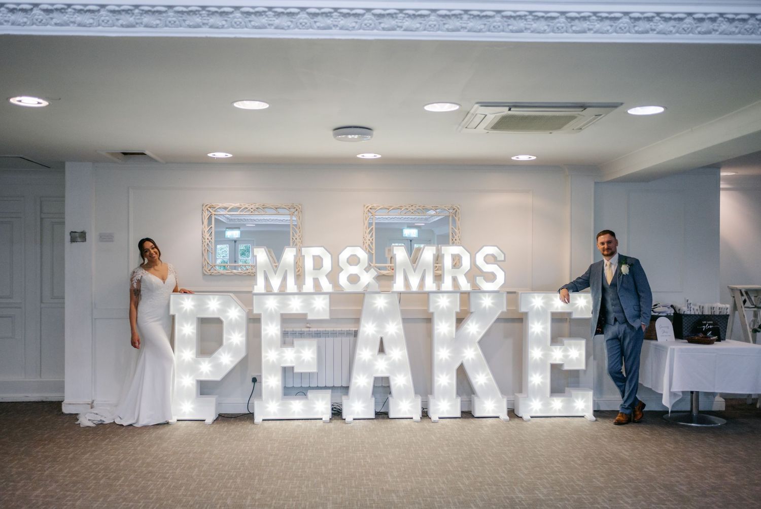 Large illuminated 'MR & MRS PEAKE' text sign displayed in a modern white event space.