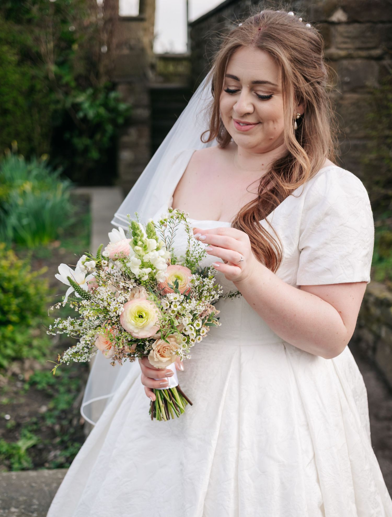 Bride in a classic white wedding dress holds a delicate bouquet of white and peach flowers.