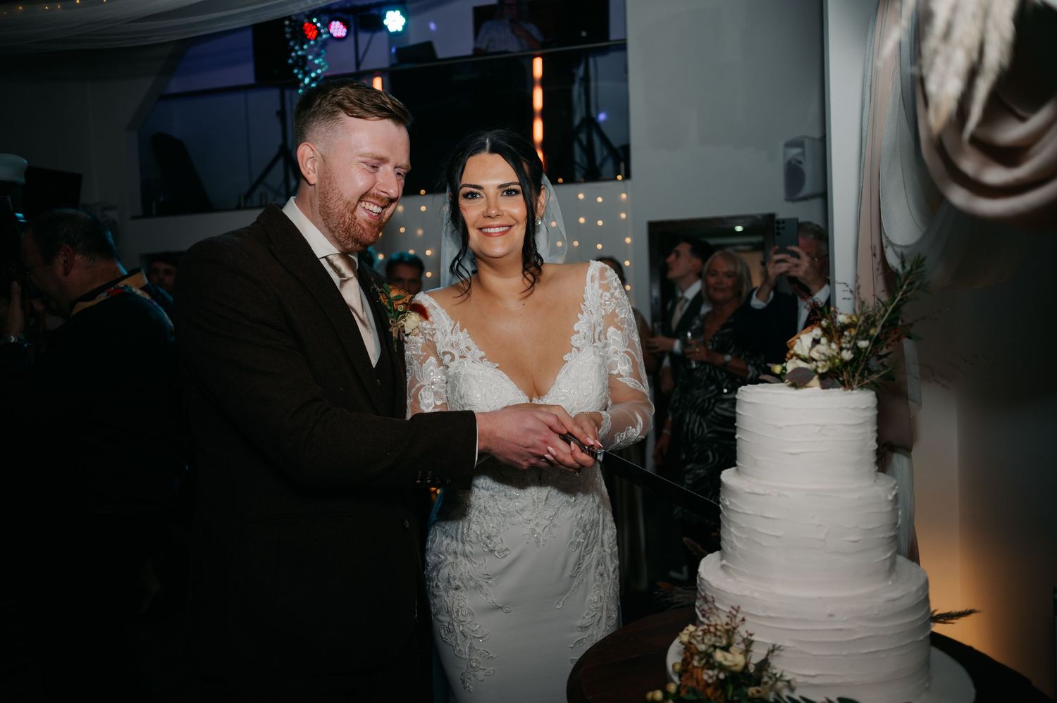 Elegant white tiered wedding cake displayed at reception with soft lighting.