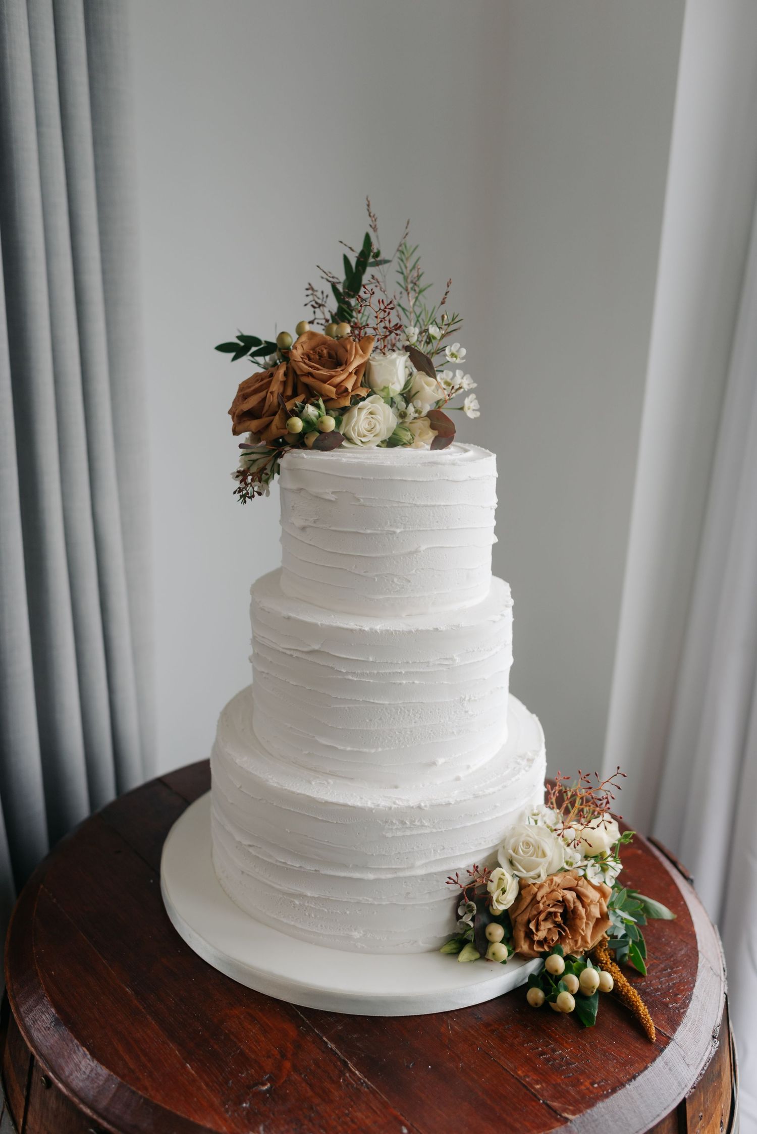 Elegant white tiered wedding cake decorated with peach-colored flowers on a wooden table.