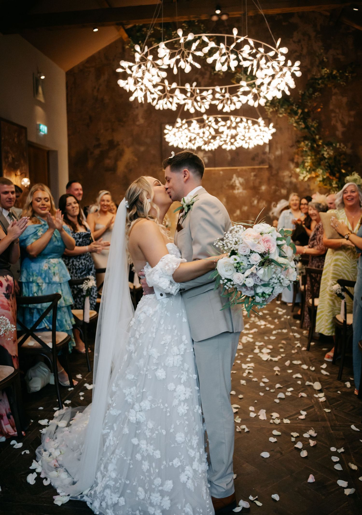Wedding couple shares first dance under illuminated floral chandeliers while guests watch.