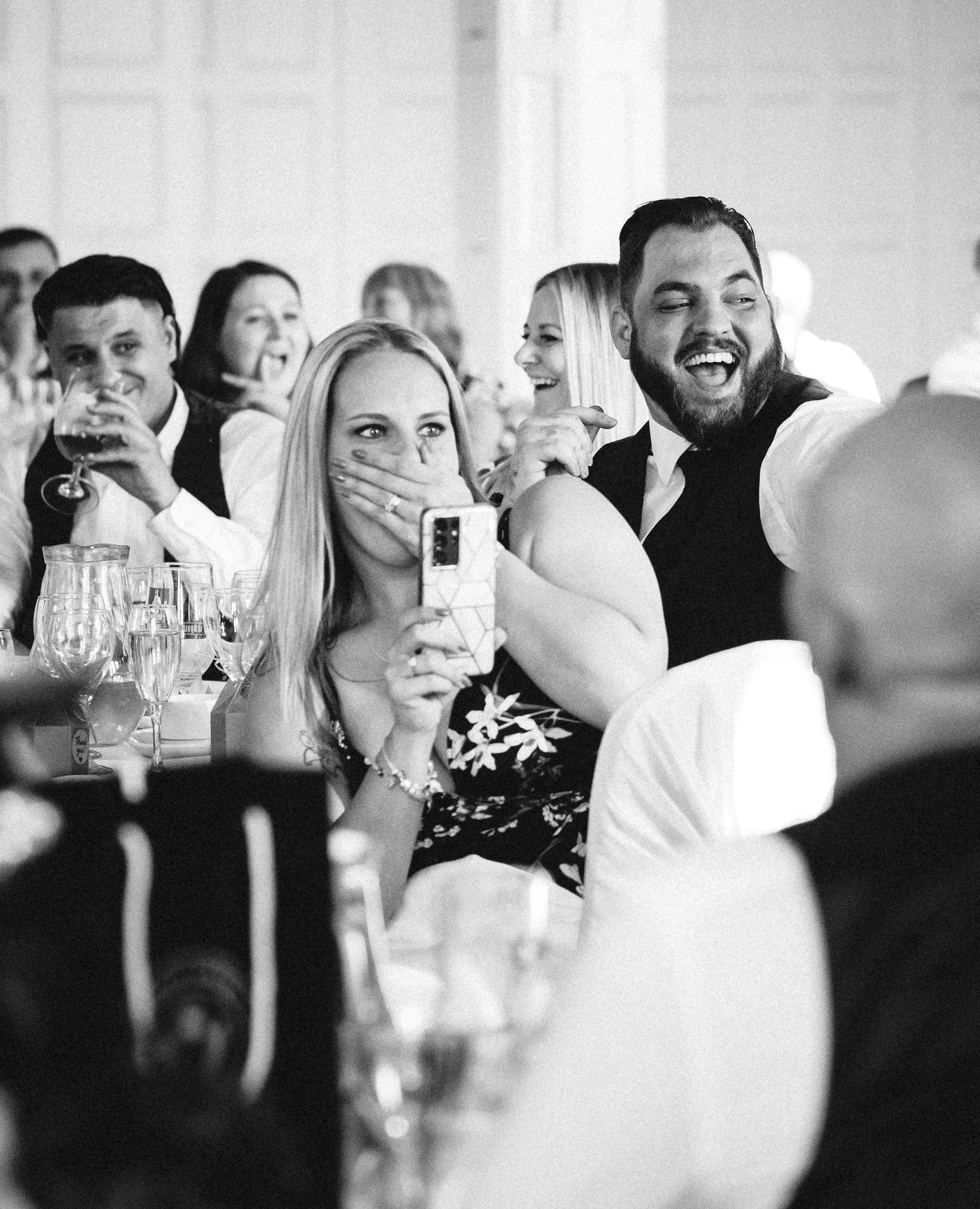 Wedding reception guests react with excitement during a celebratory moment in black and white.