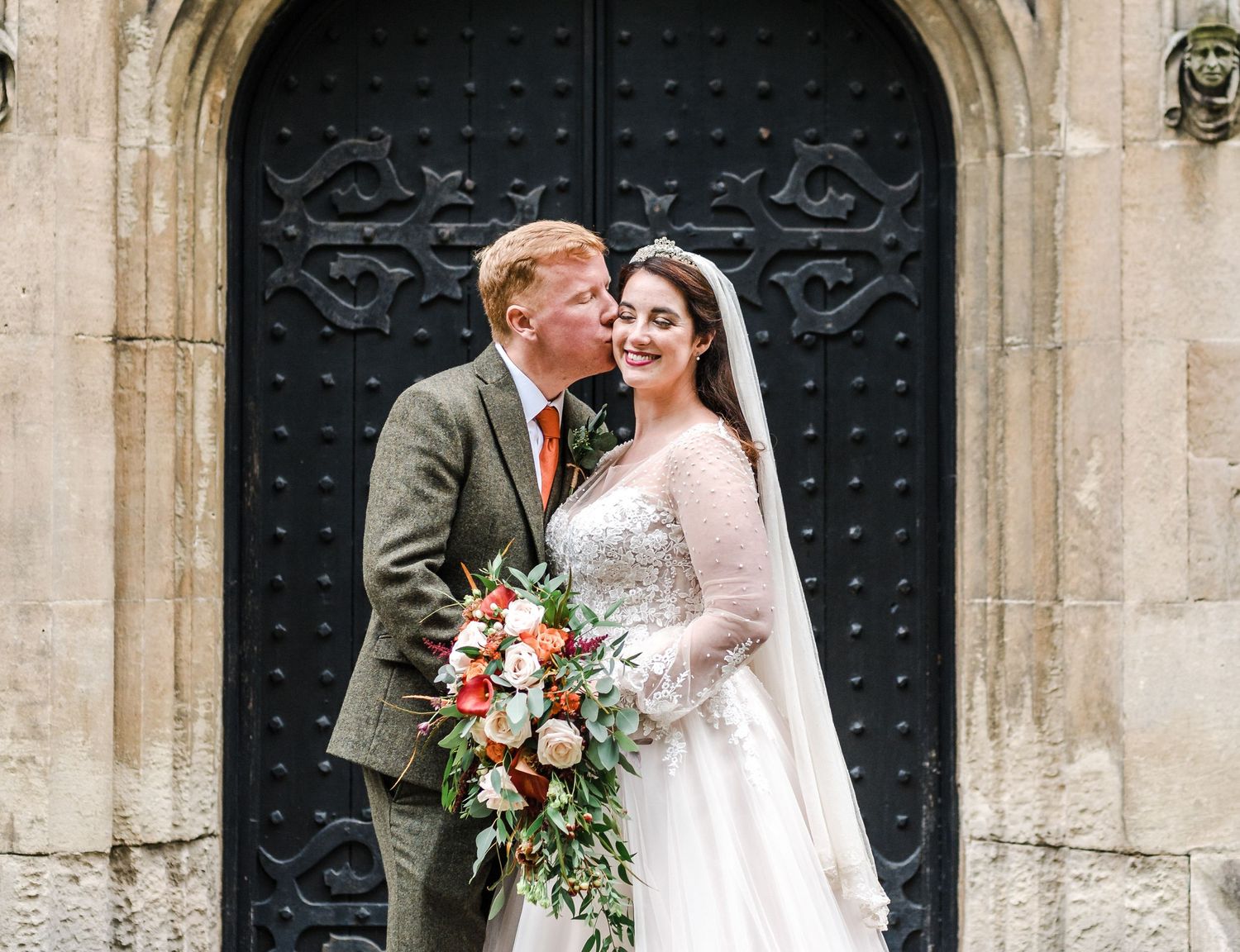 Happy couple shares an intimate moment in front of a gothic church doorway.