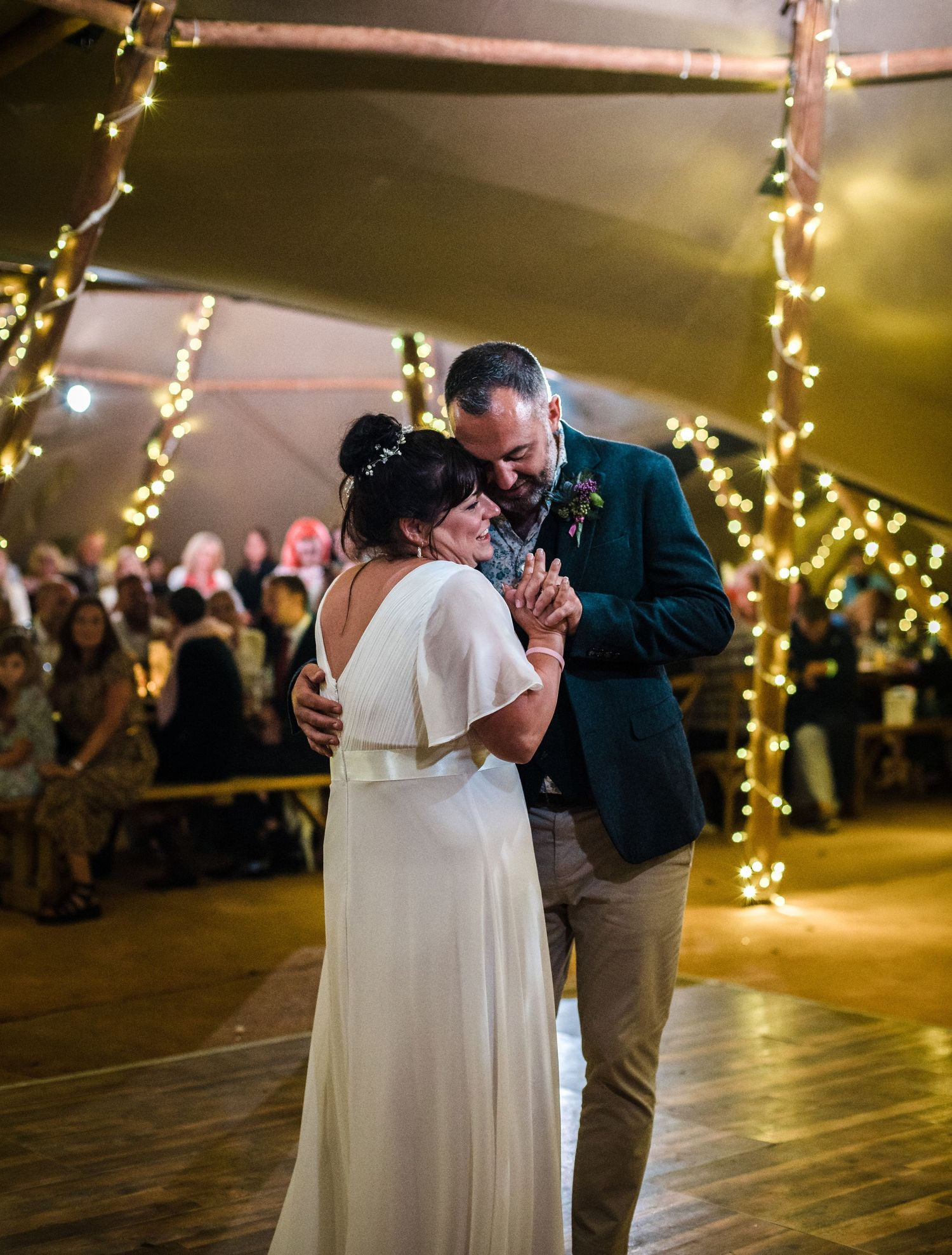 A couple sharing a romantic dance moment under string lights at their wedding reception.
