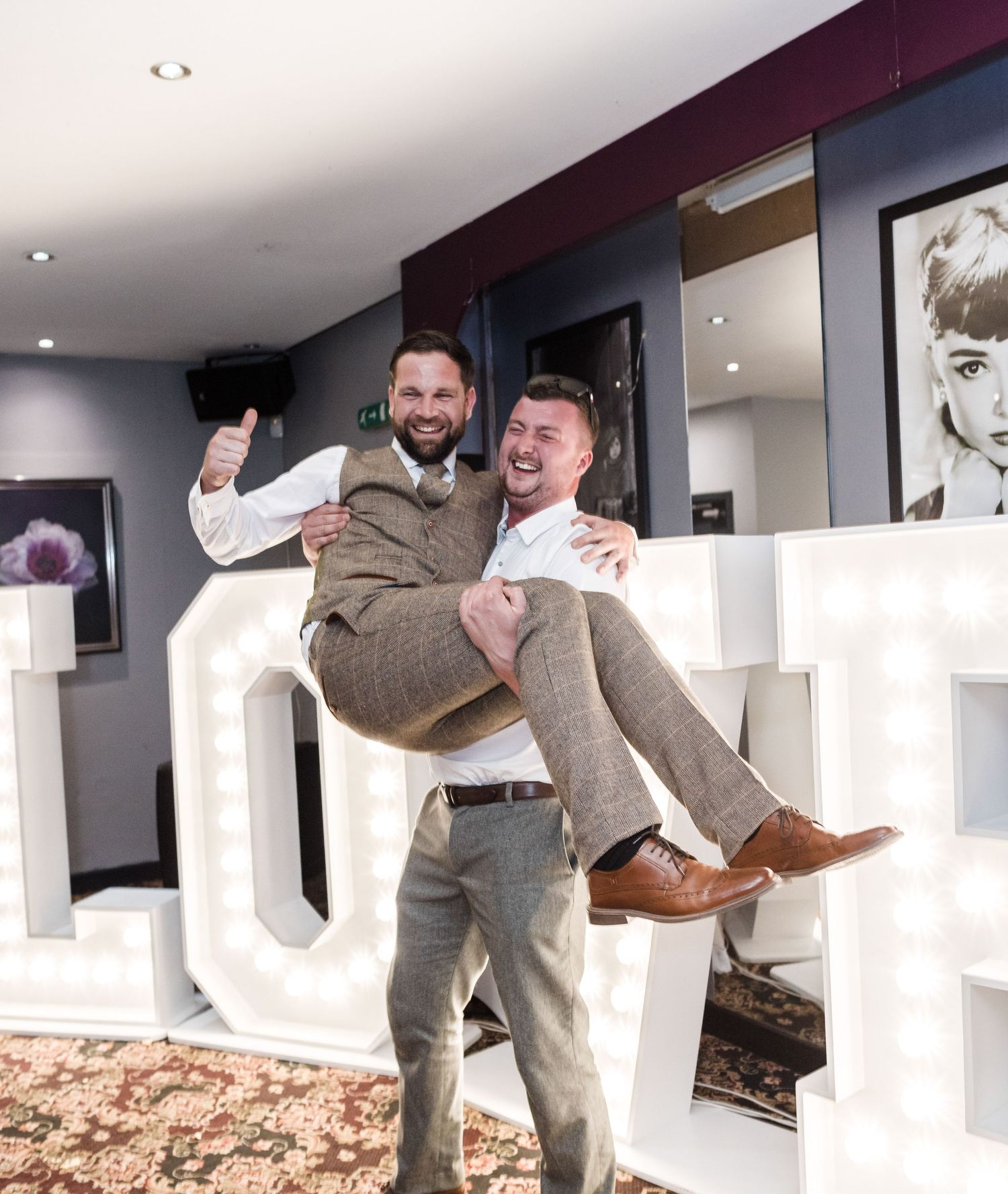 Two guests playfully pose on decorative LOVE letters at a wedding reception.