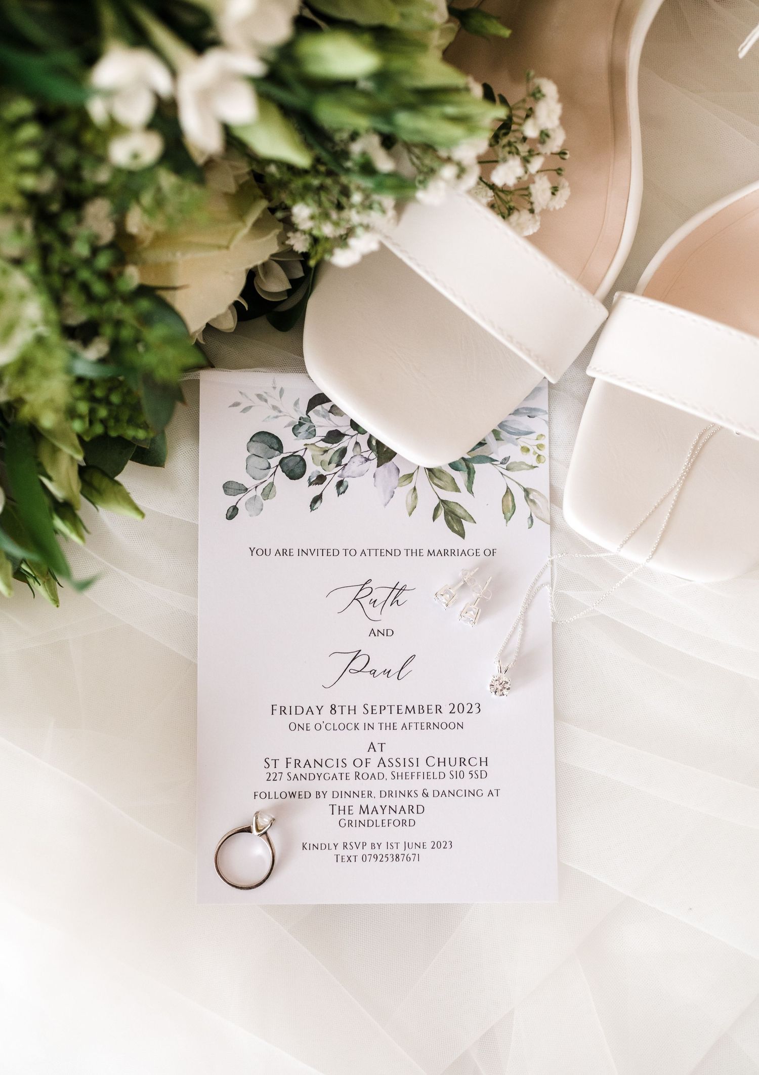 Wedding invitation with floral design alongside bridal shoes and fresh flowers.