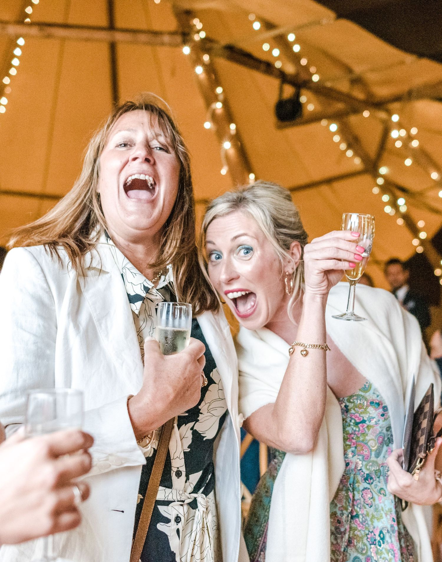Candid moment of guests laughing and celebrating with drinks at wedding reception.