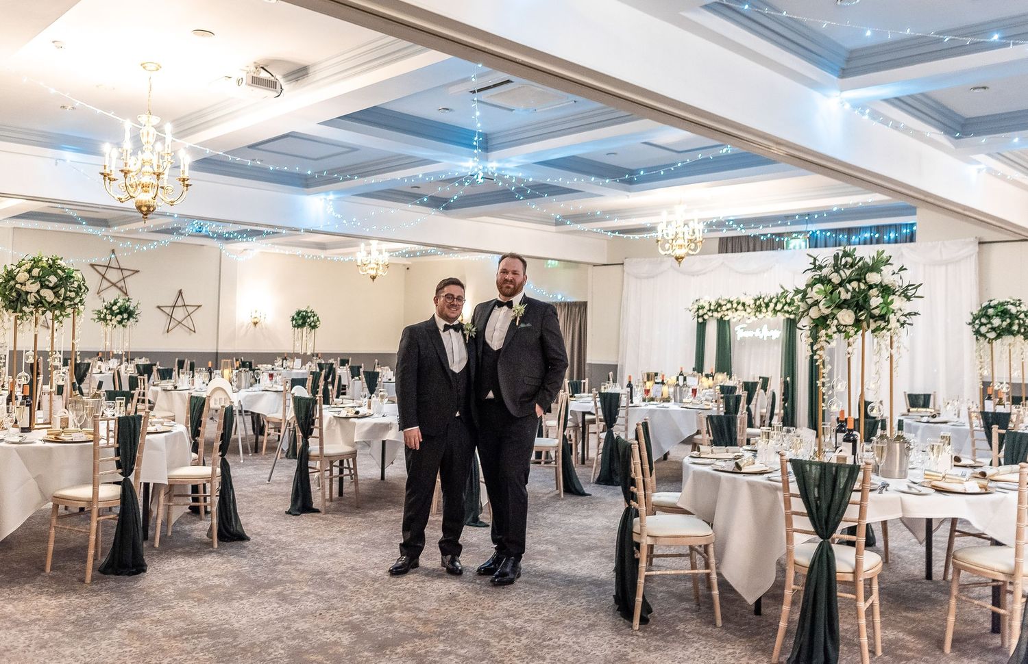 Elegant wedding reception hall with coffered ceiling, crystal chandeliers and beautifully decorated round tables.