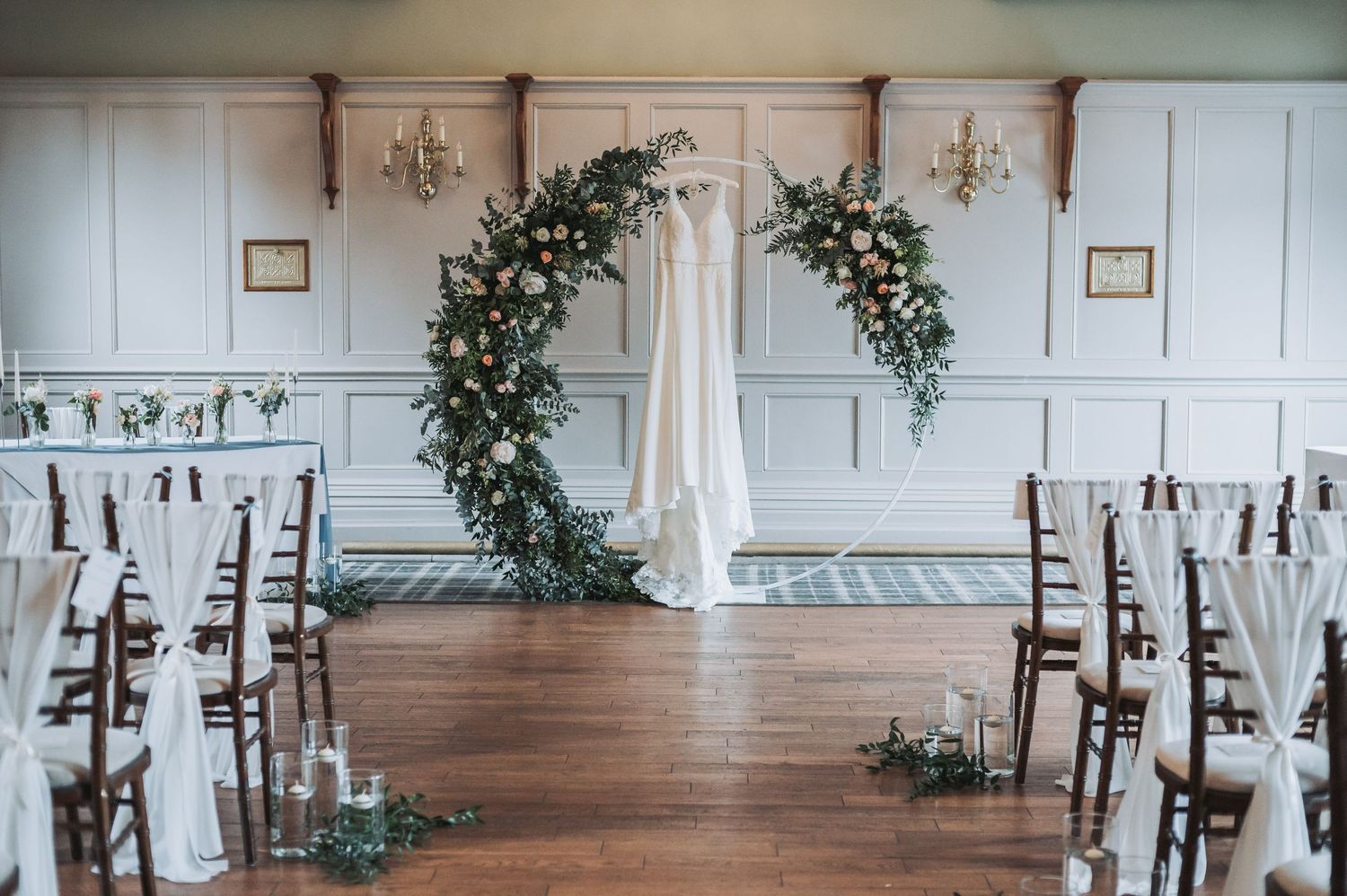 Elegant wedding ceremony setup with a circular floral arch and white chairs in a classic indoor venue.