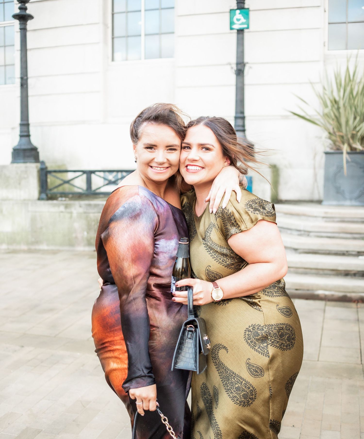 Two guests in elegant dresses share a warm embrace at formal event.