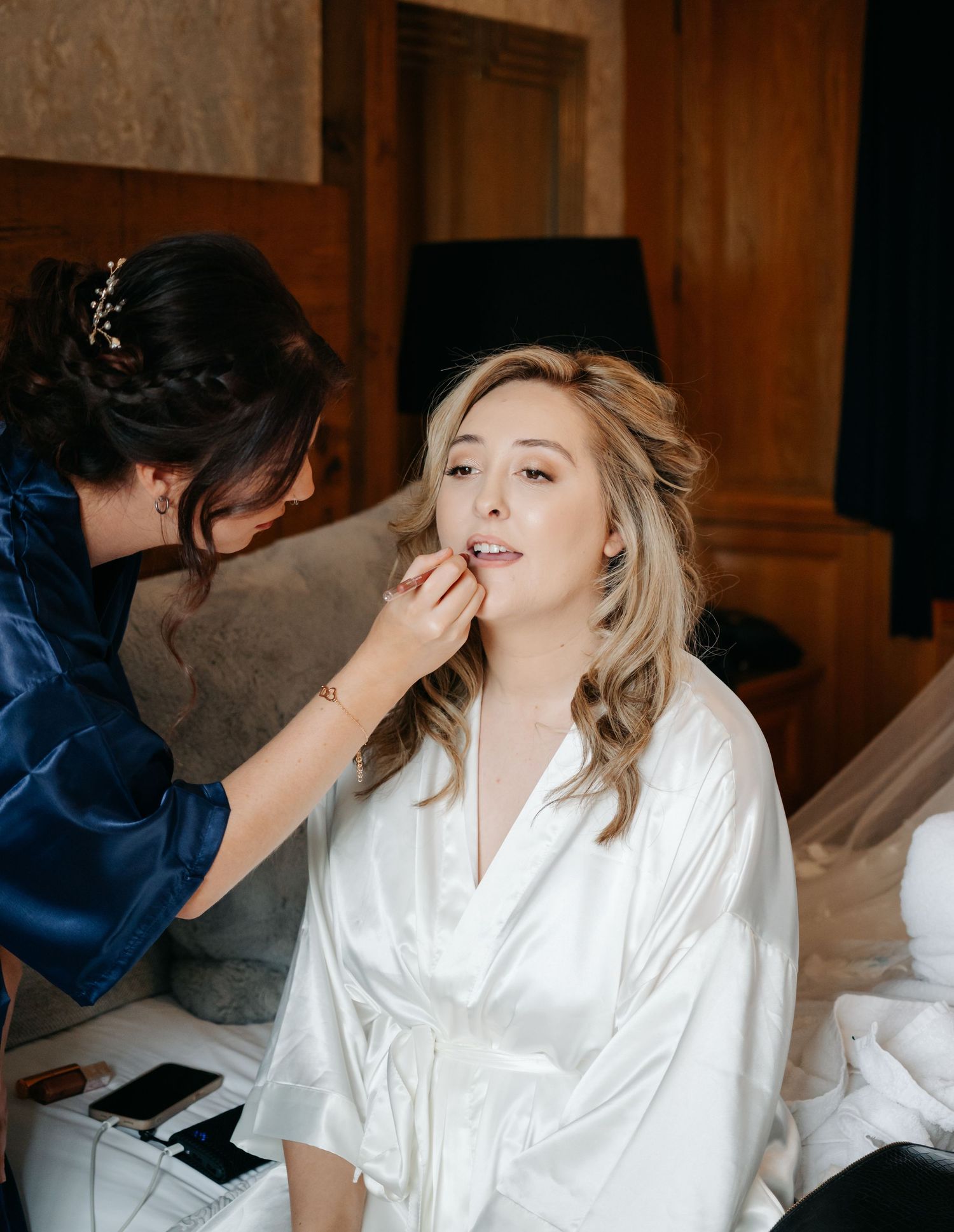 A makeup artist applies cosmetics to a person wearing a white silk robe during wedding preparations.