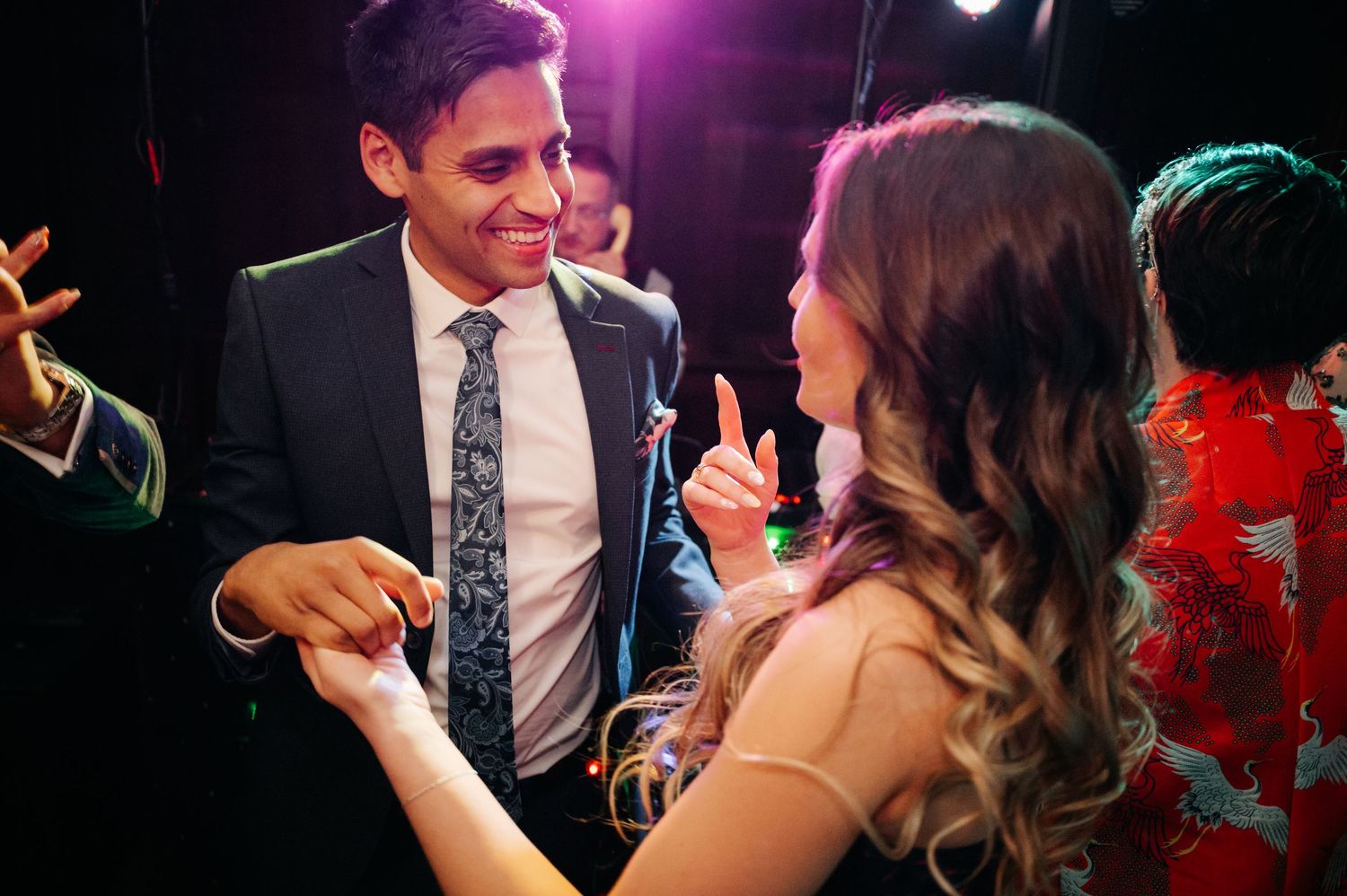 Wedding guests dancing together at an evening reception with colorful lighting.