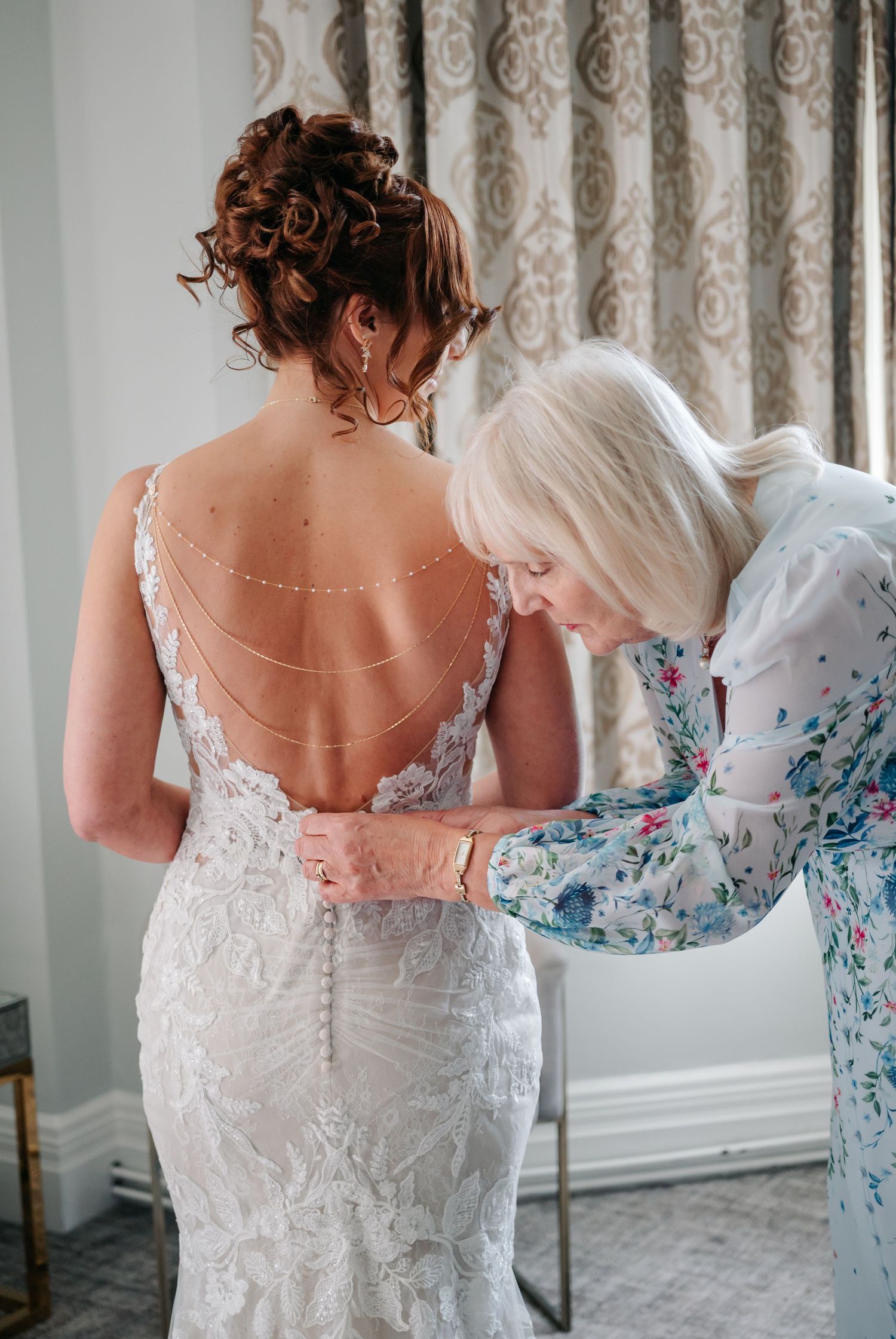 Assistants help adjust the back of an elegant white lace wedding gown with delicate button details.