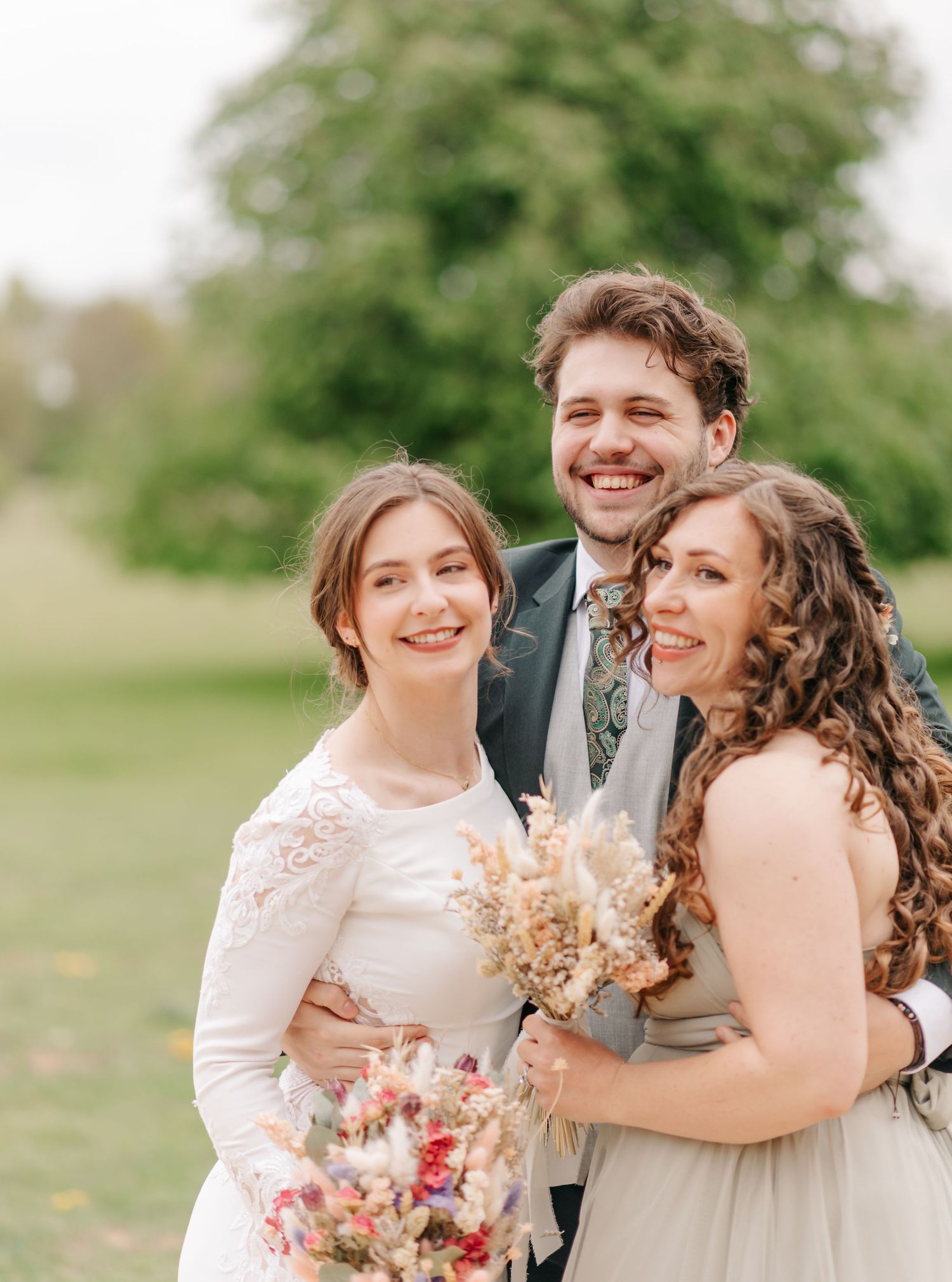 Joyful wedding party poses outdoors with spring flowers and natural greenery.