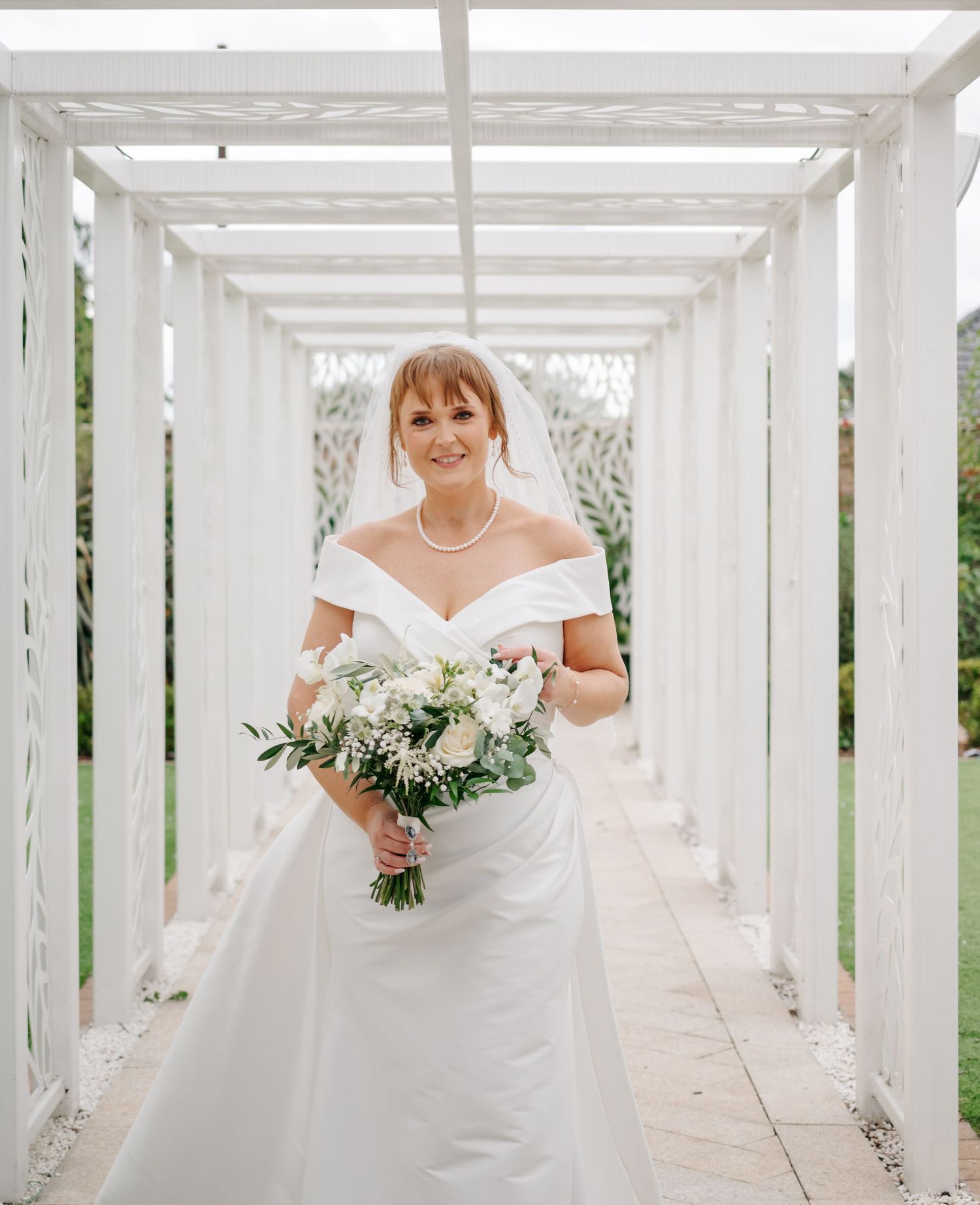 A white pergola walkway creates an elegant bridal portrait setting with natural light.