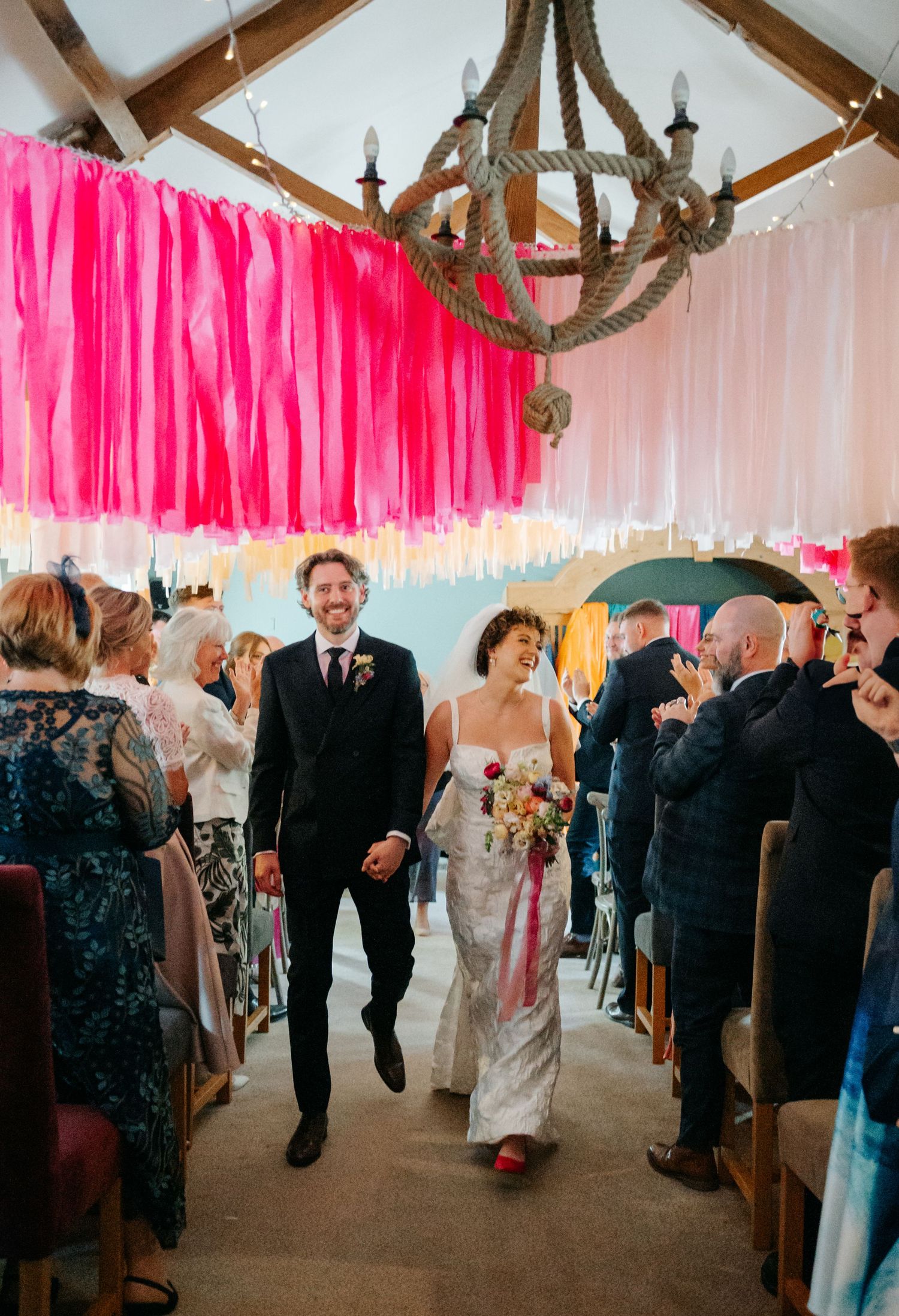 Wedding reception venue decorated with pink streamers and rustic wooden beams overhead.