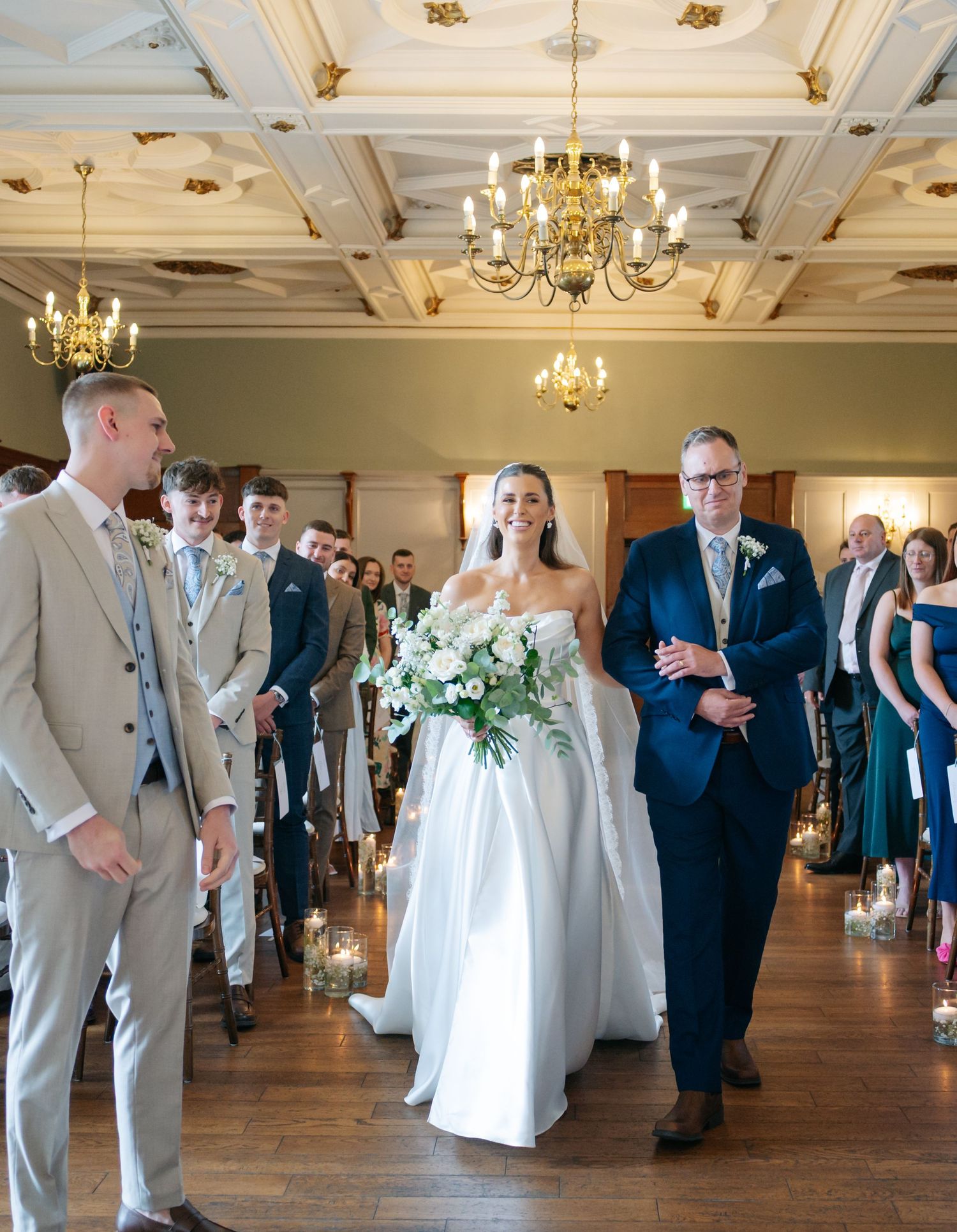 Wedding guests dance in an elegant ballroom with ornate chandeliers and coffered ceiling.
