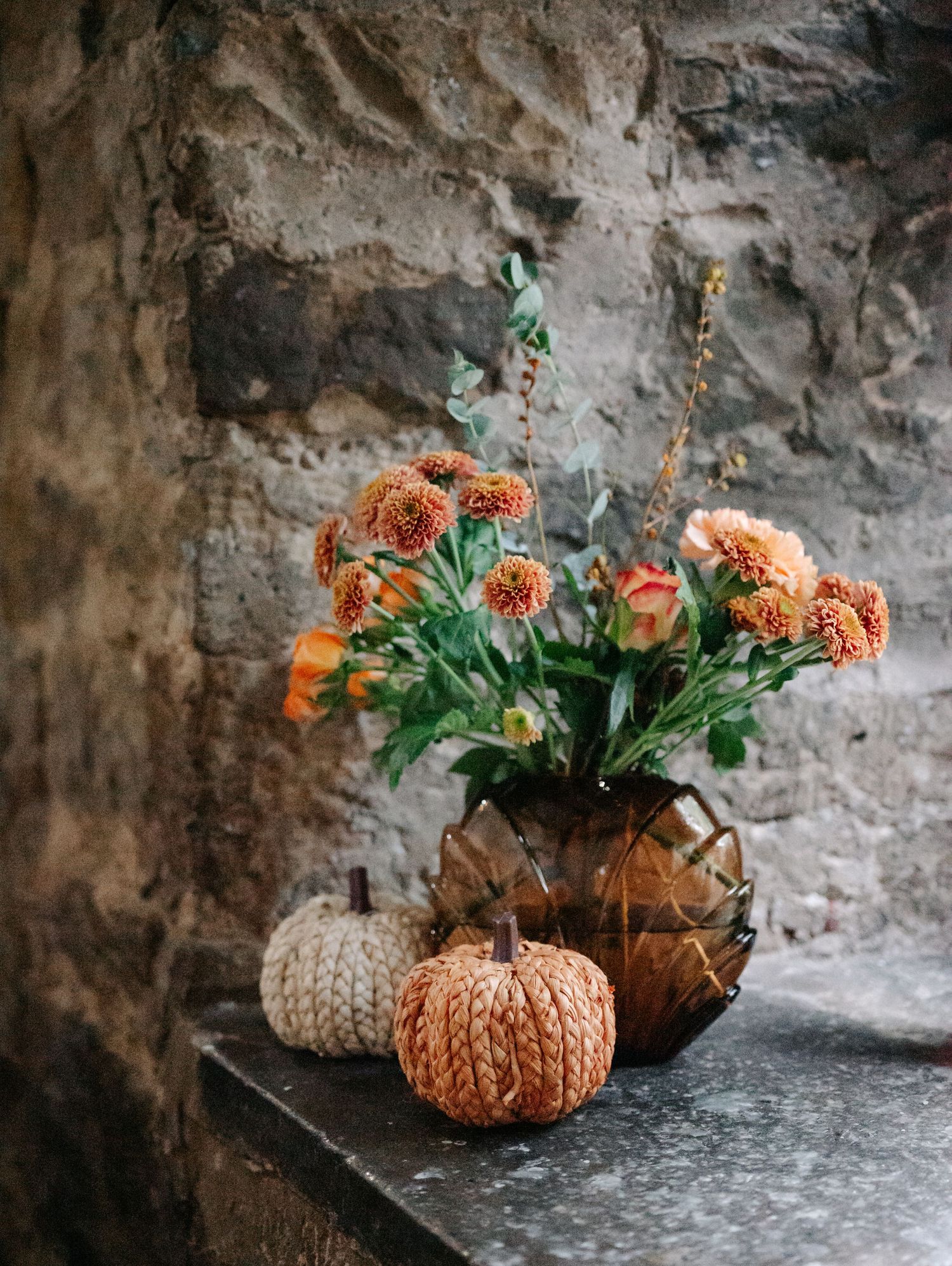 Rustic autumn decorations featuring orange ceramic pumpkins and greenery against a stone wall.