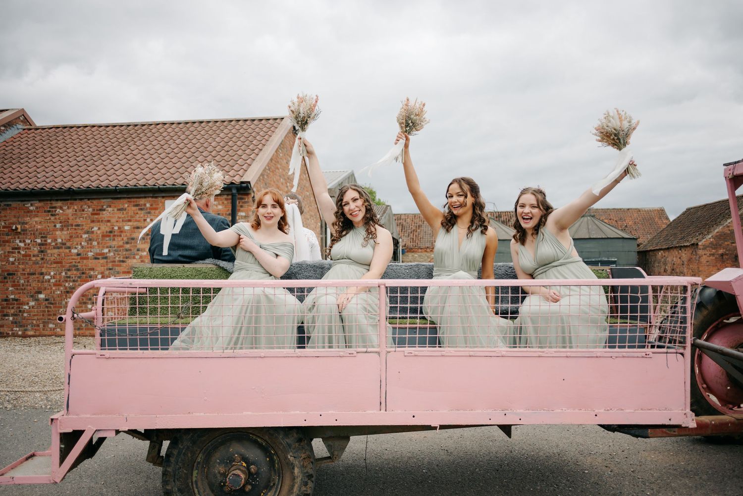Wedding party members sit on a pink vintage car showing joyful expressions.