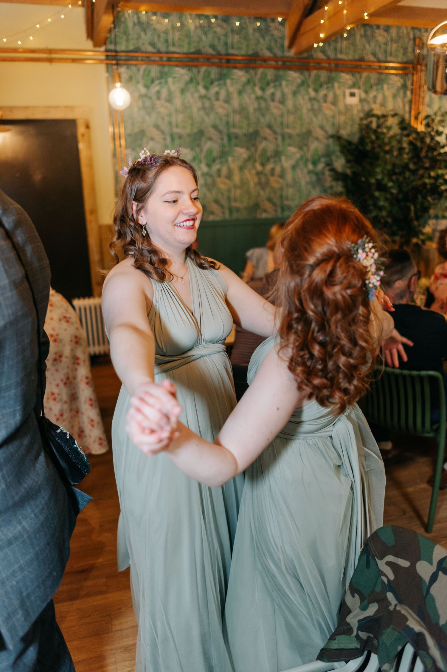 Wedding guests in sage green dresses dancing and celebrating at indoor reception.