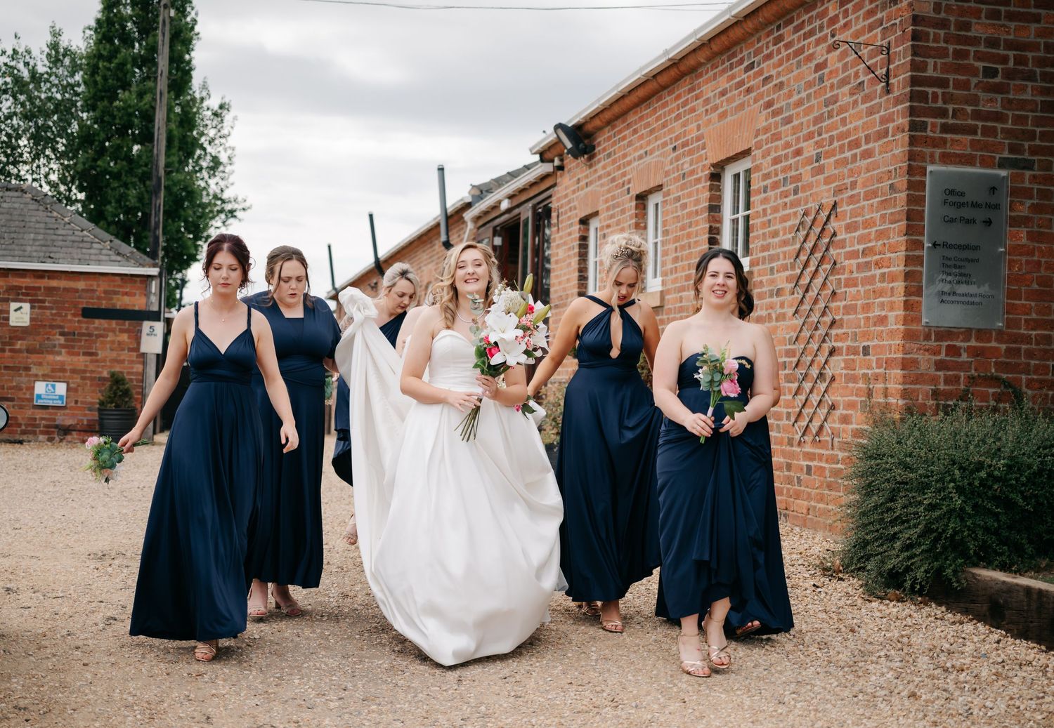 Wedding party in navy blue dresses and white gown pose together against a brick building exterior.