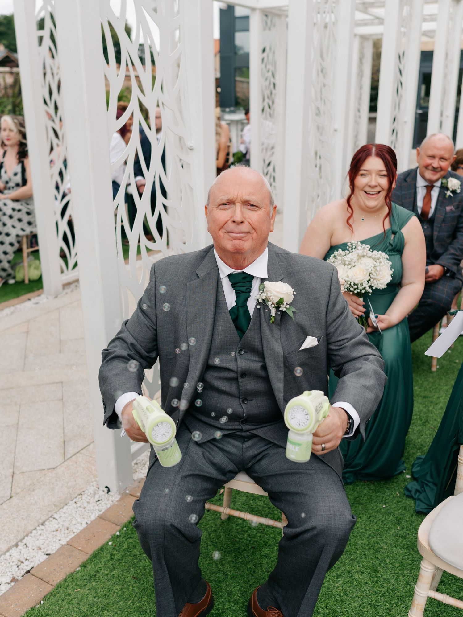 Wedding party poses behind decorative white lattice panels with greenery in an outdoor garden setting.