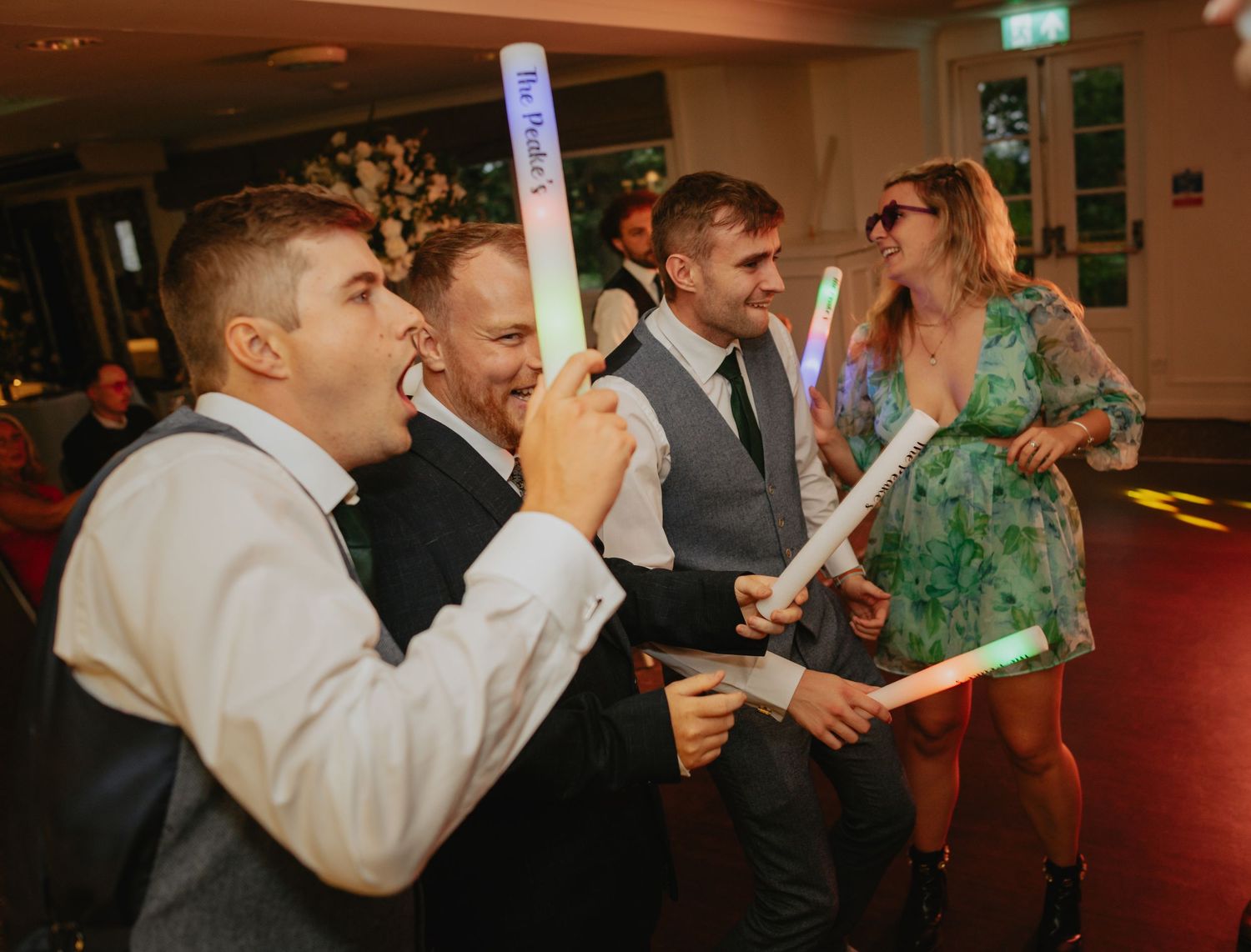 Wedding guests celebrate with glow sticks on darkened dance floor.