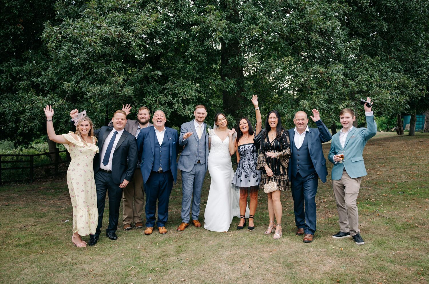 Large group wedding photo taken outdoors with guests gathered on grass.