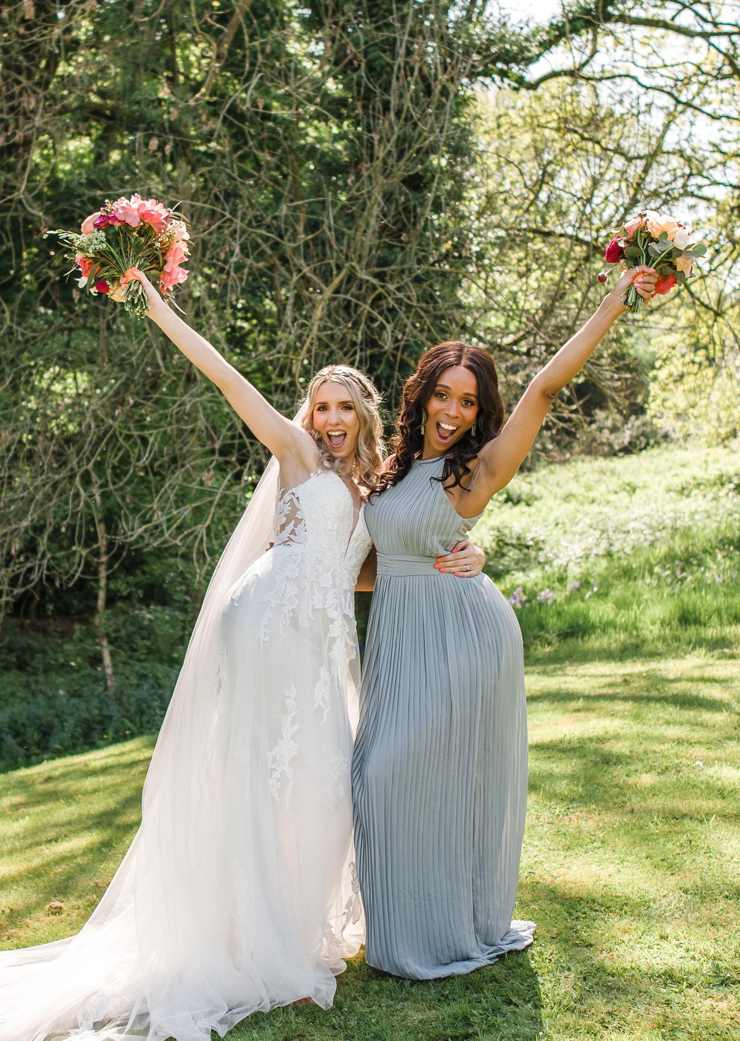 Celebratory pose with raised bouquets against lush garden backdrop.