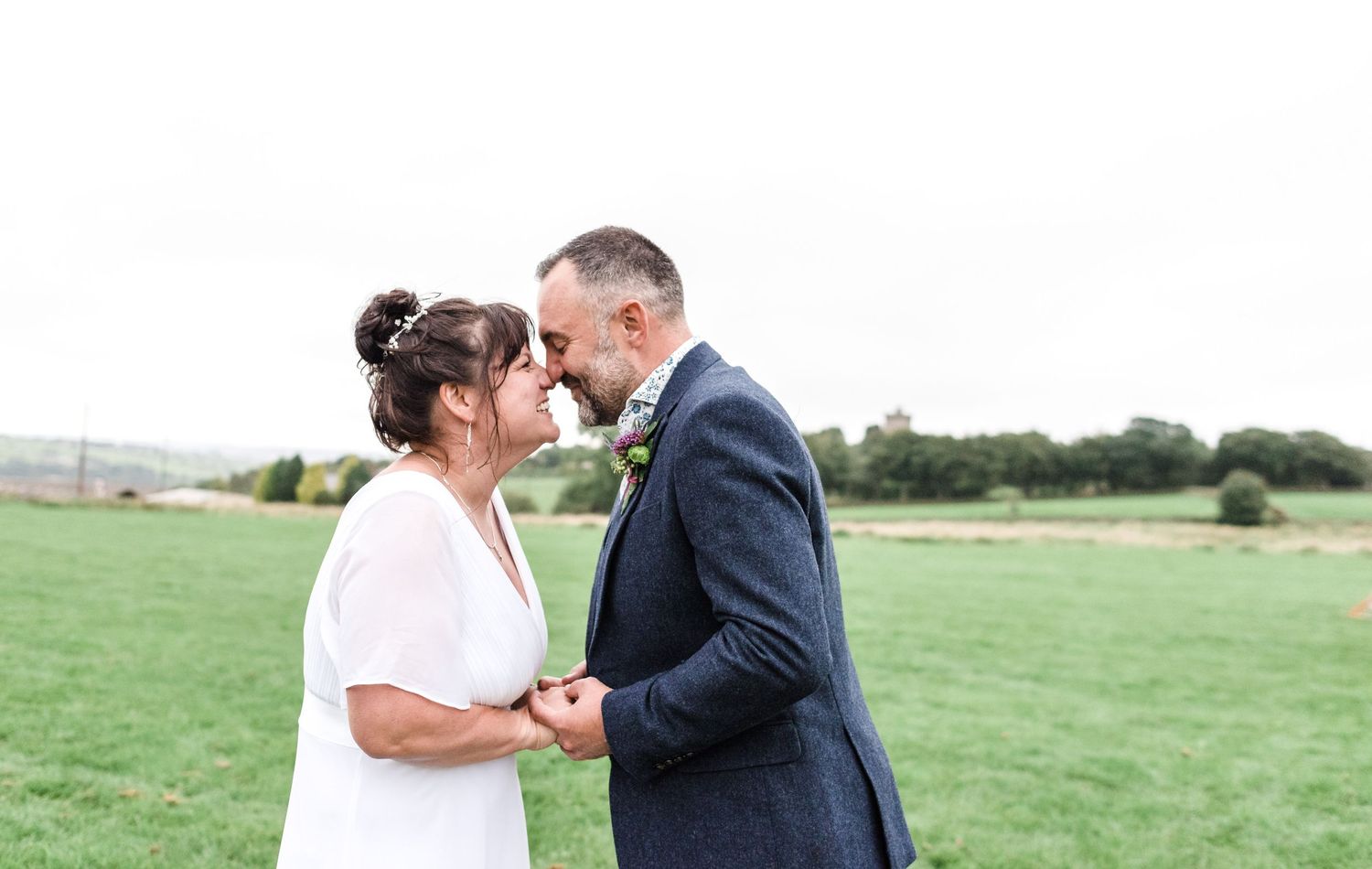 Romantic outdoor wedding portrait in a green field with a tender moment between newlyweds.