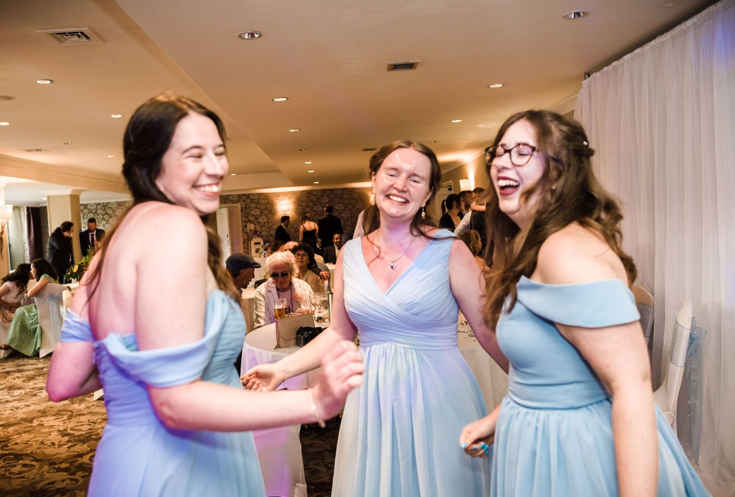 Bridesmaids in pastel blue dresses share a joyful moment during wedding reception.