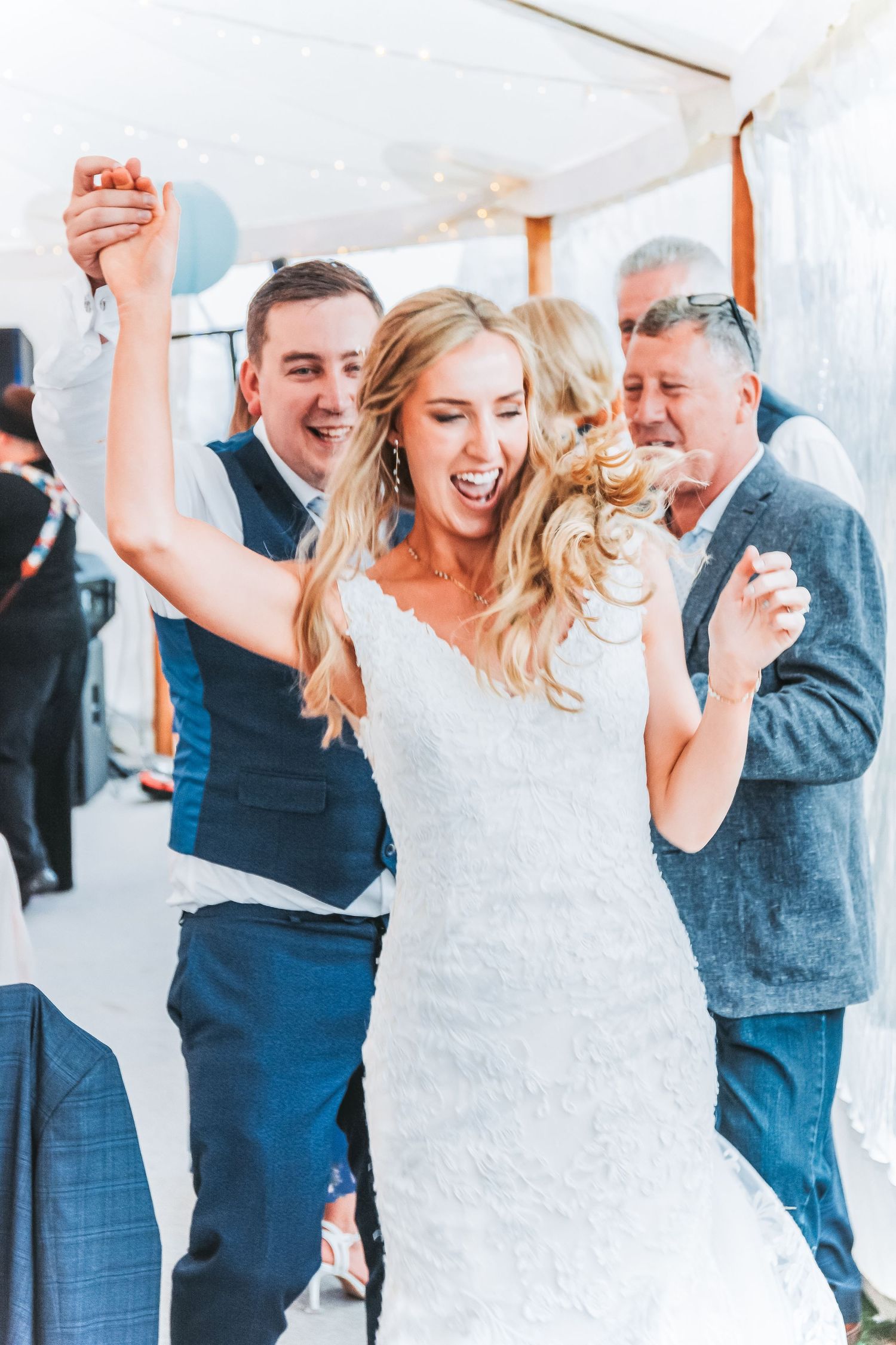 Joyful celebration during wedding reception under white tent with blue lanterns.
