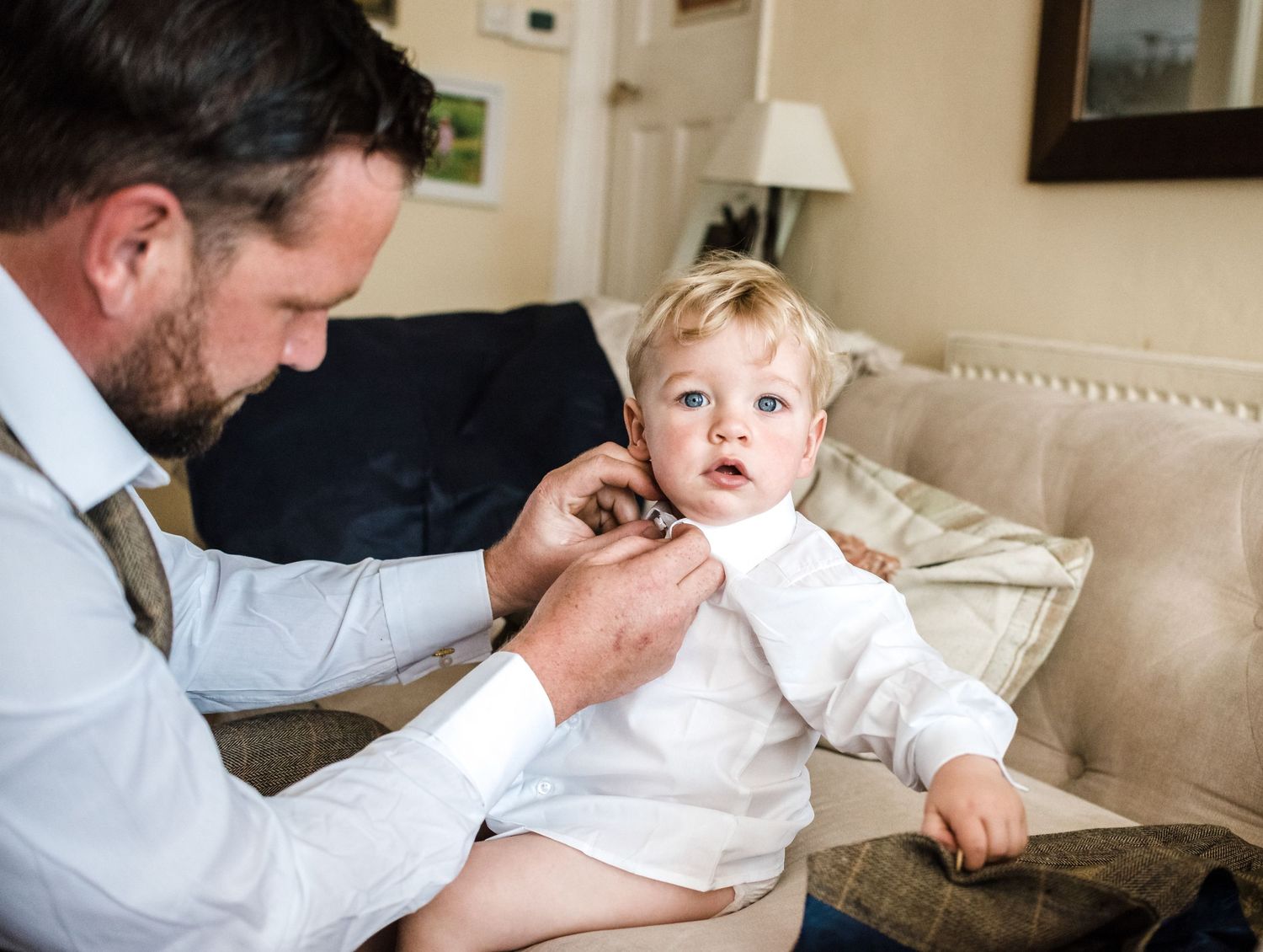 Intimate moment of wedding preparation with child getting dressed in white shirt.