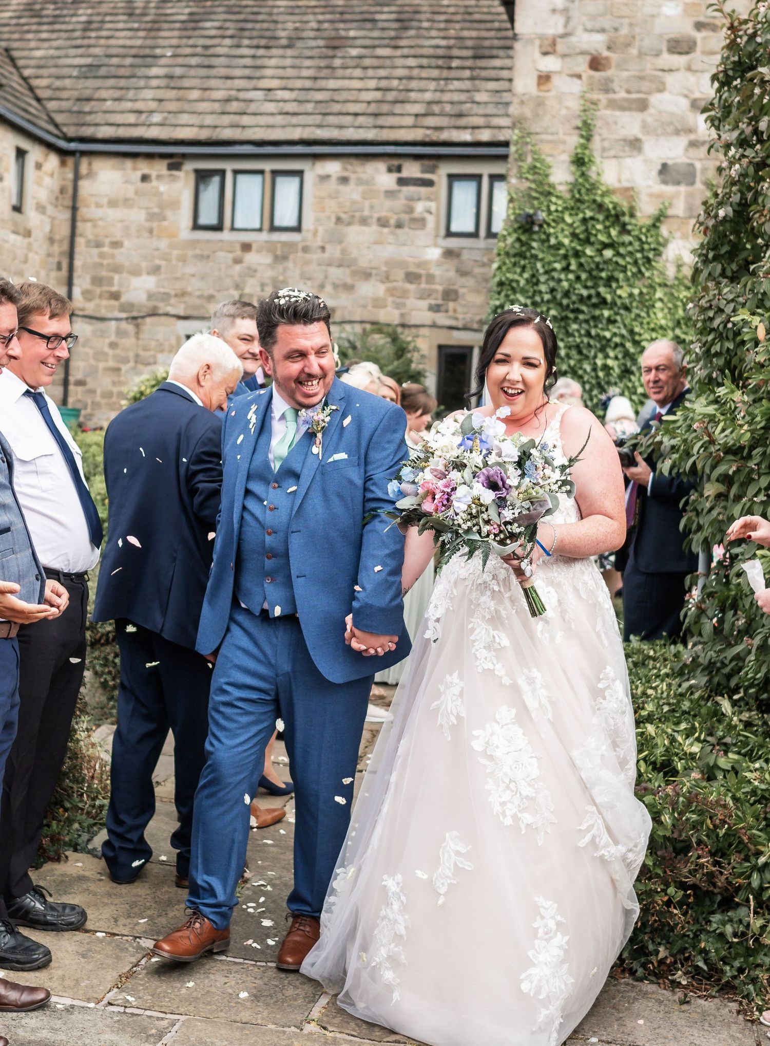 A couple celebrates with joy outside a stone building as confetti falls during their wedding ceremony.