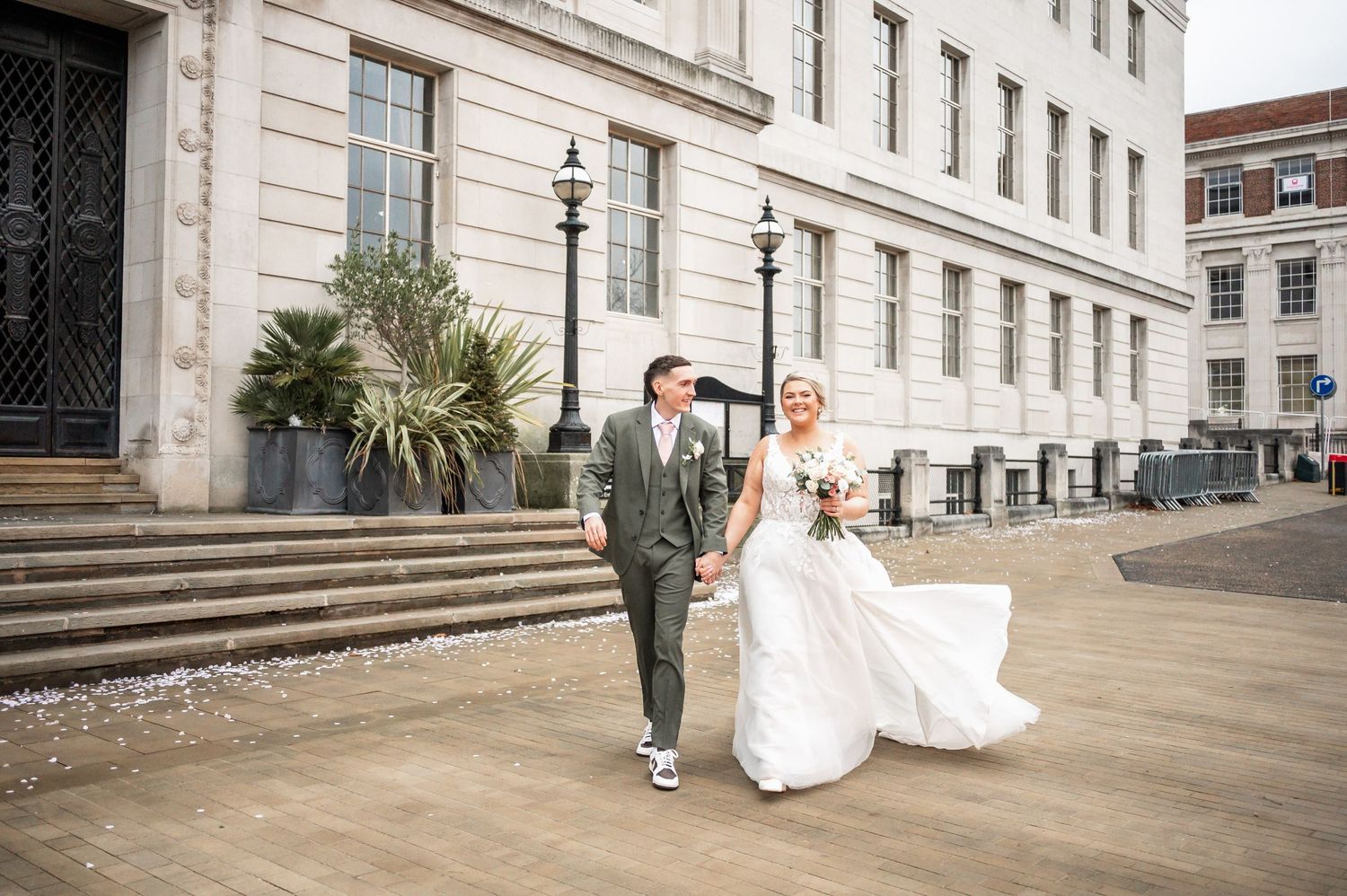 Couple walks along historic building exterior with palm plants and stone steps in background.