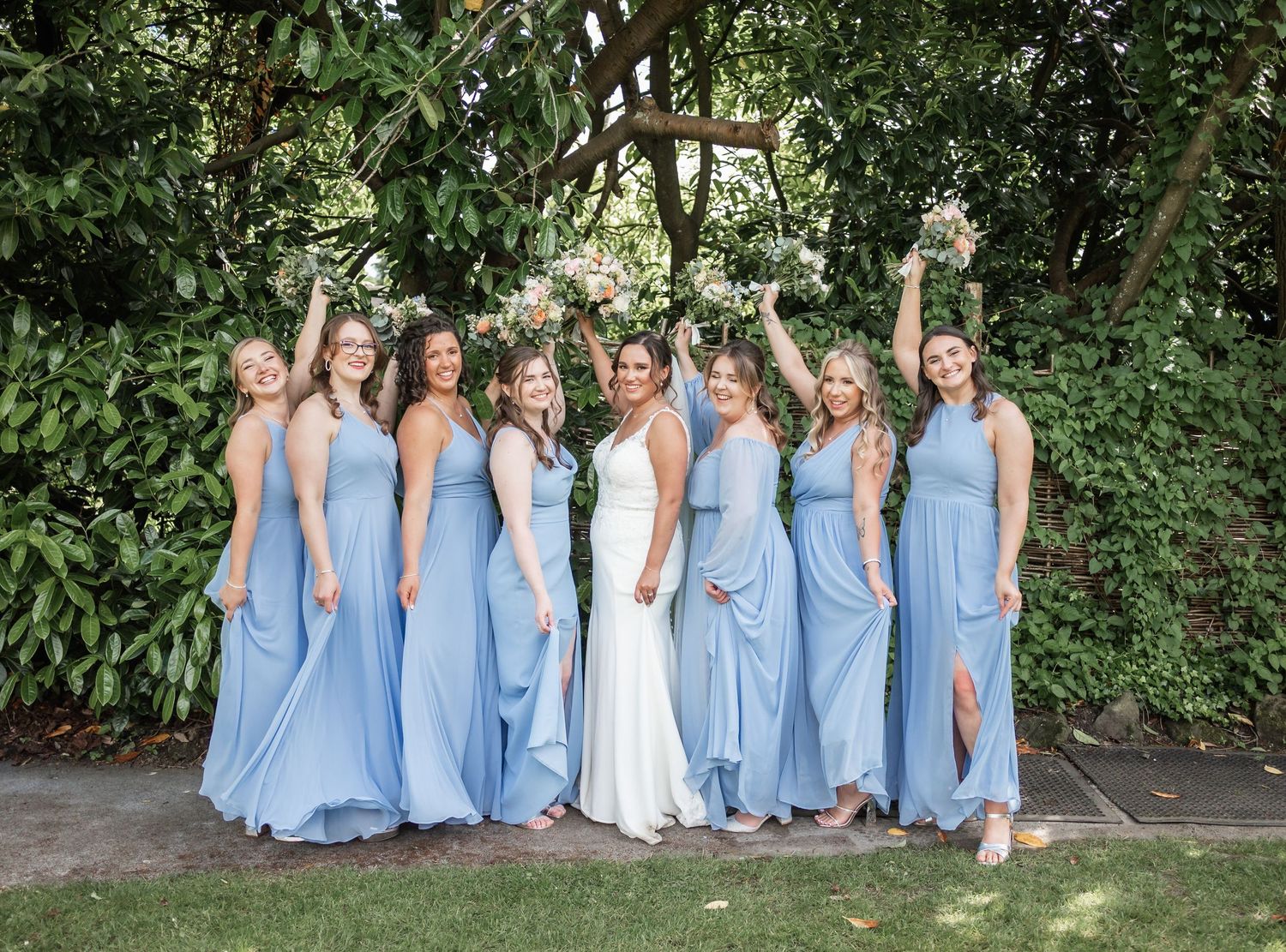 Wedding party posed outdoors with bridesmaids in matching light blue dresses standing with the bride.