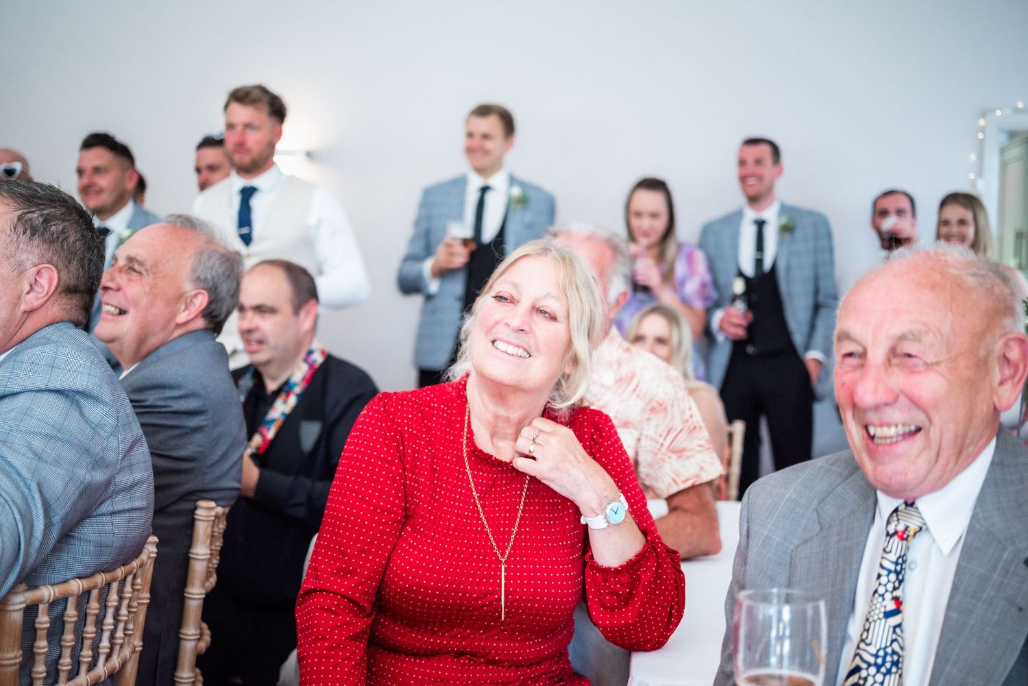 Wedding guests laughing during reception speeches in elegant venue setting.
