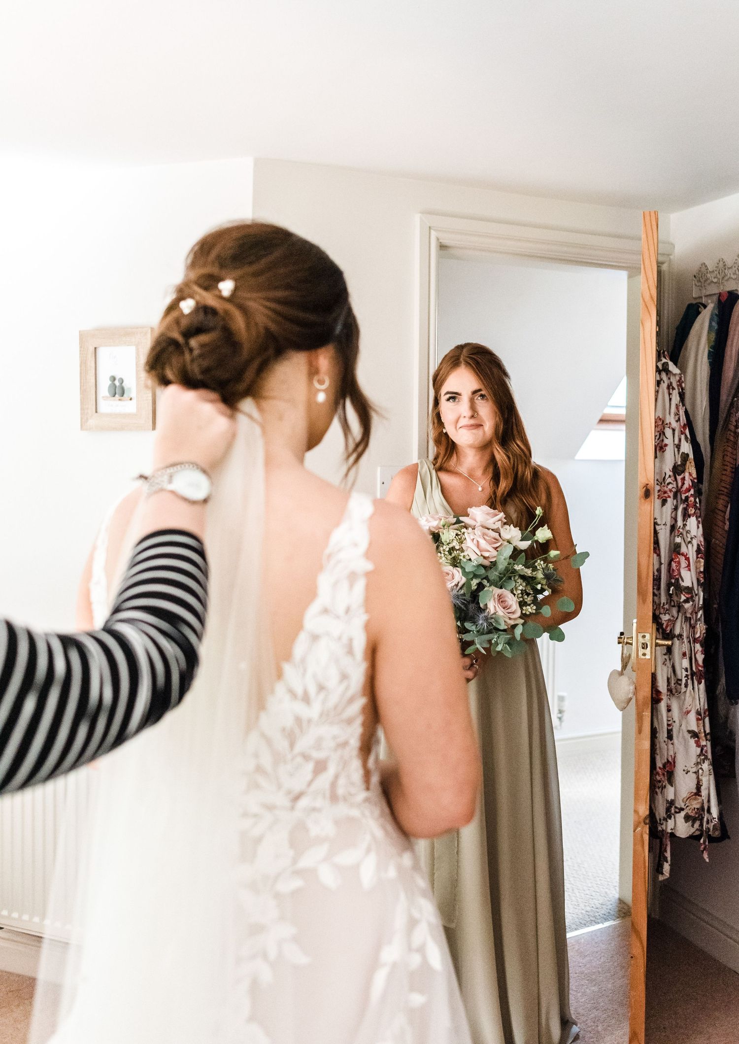 Tender moment captured as bridesmaid in sage green dress holds floral bouquet during wedding preparations.