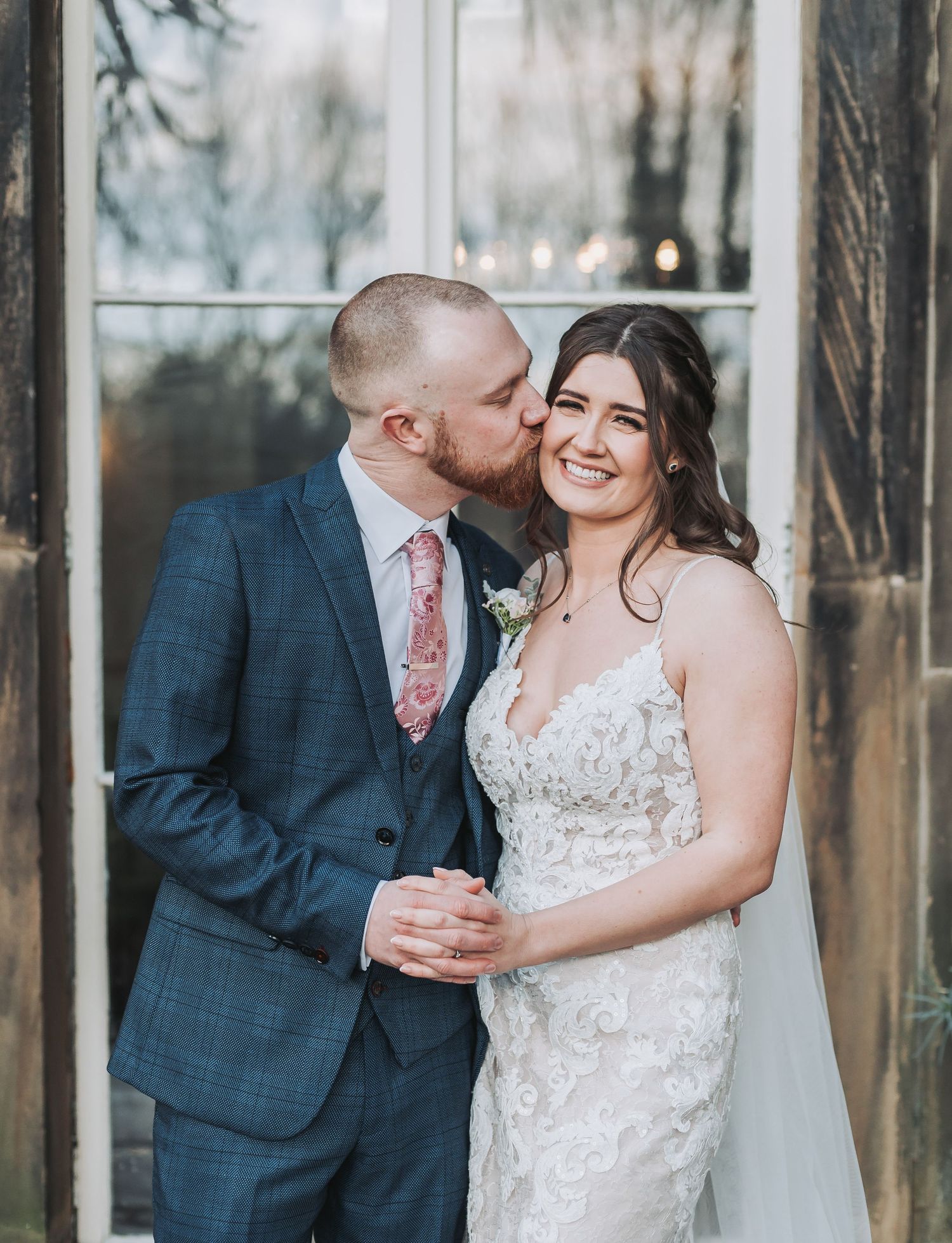 A romantic moment between newlyweds near a window in formal attire.