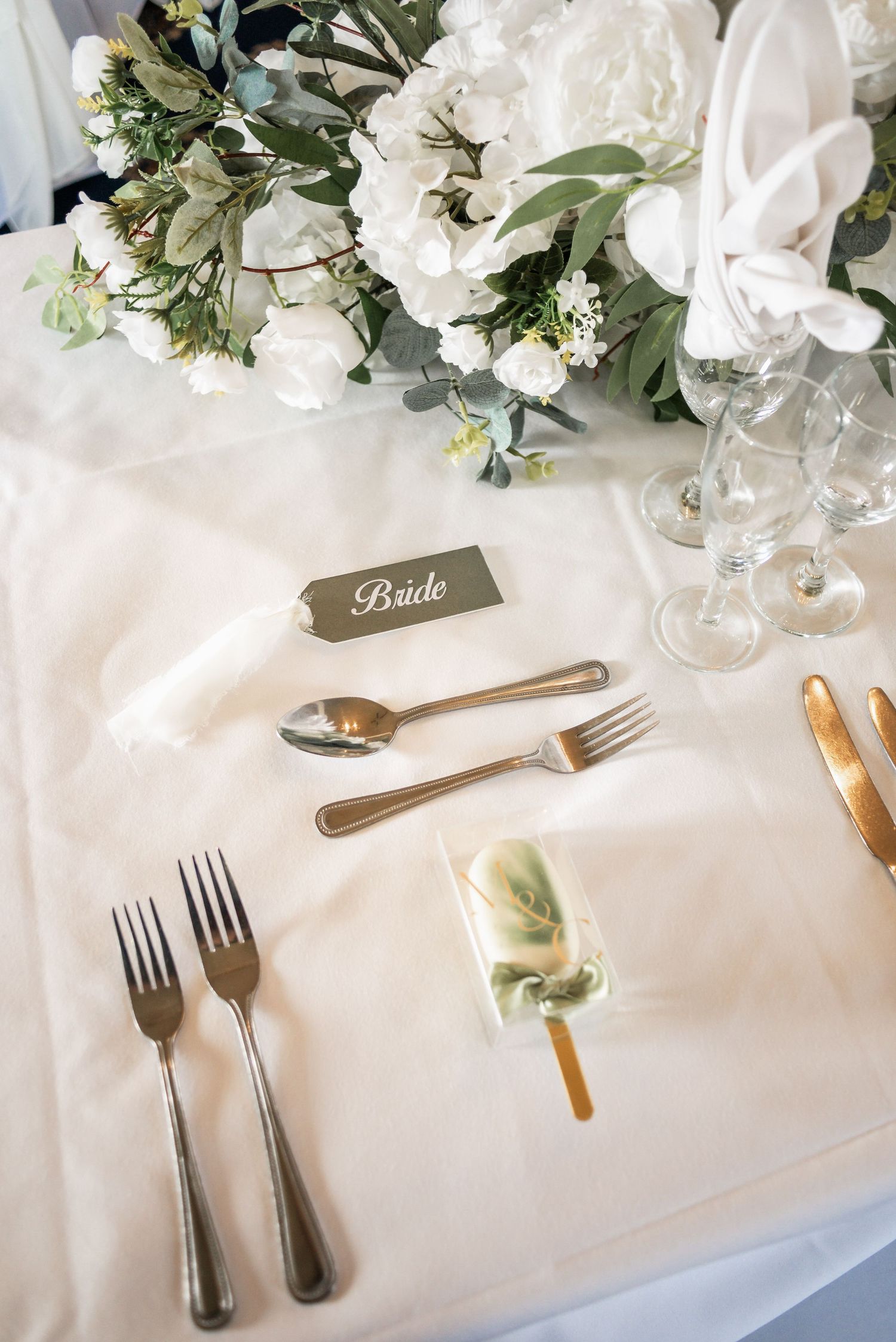 Place setting detail with white florals and 'Bride' name card at wedding reception.