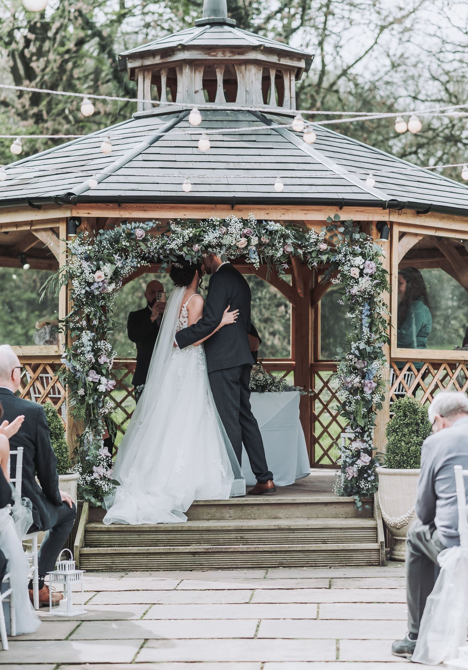A wedding ceremony in progress inside a decorated octagonal gazebo with guests watching.