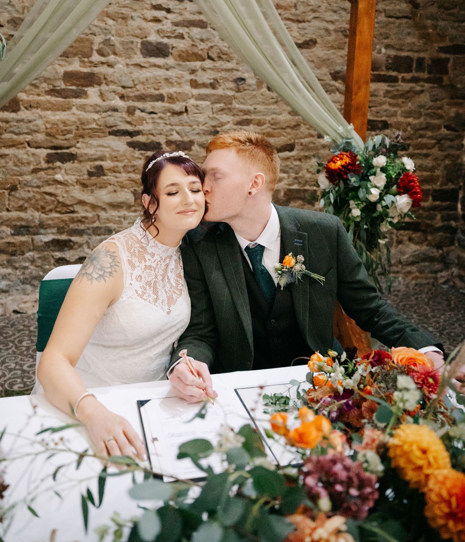 A couple signs marriage documents at a table decorated with colorful autumn flowers.