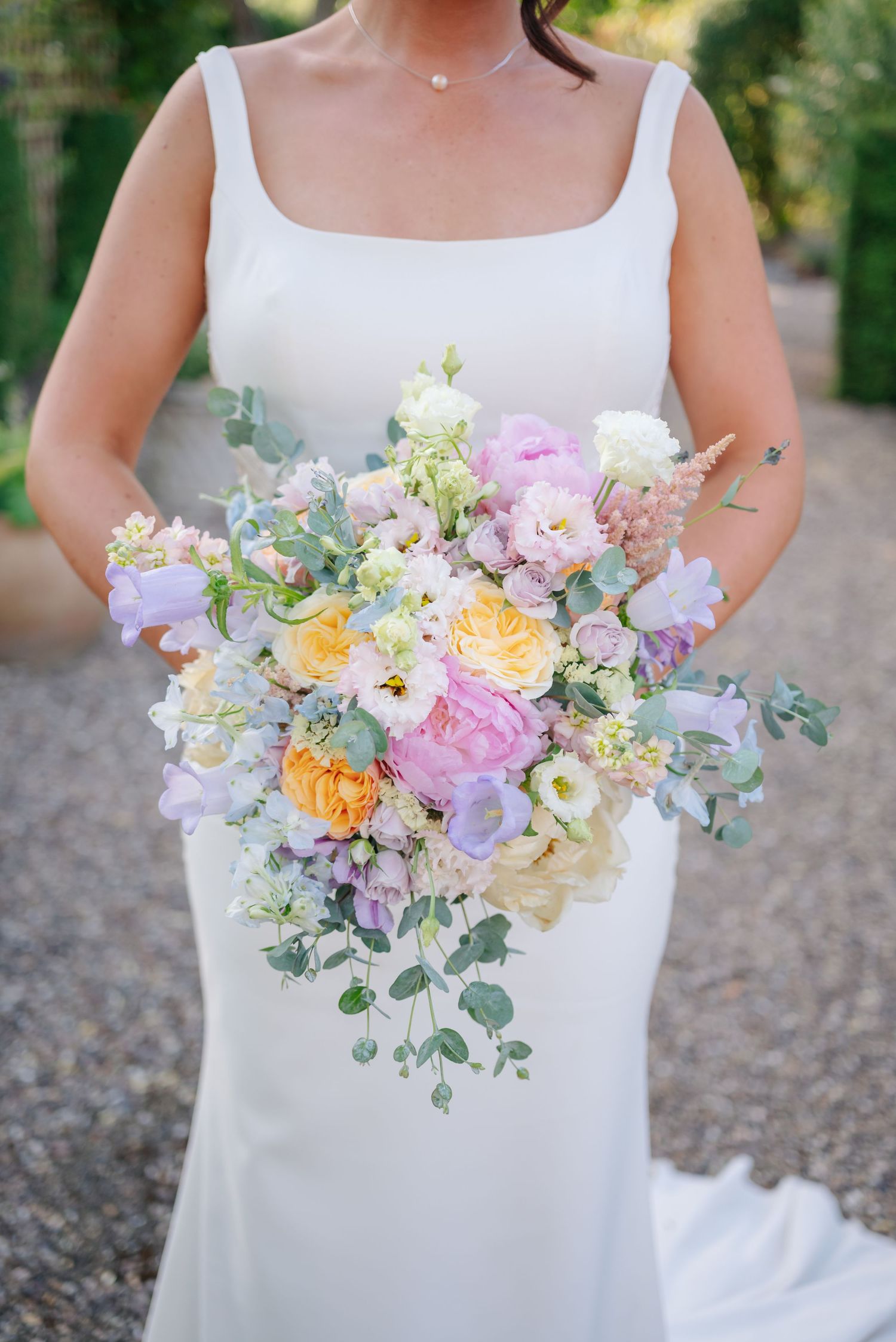 Elegant pastel bouquet with pink, yellow and white flowers held against a white dress at a wedding.