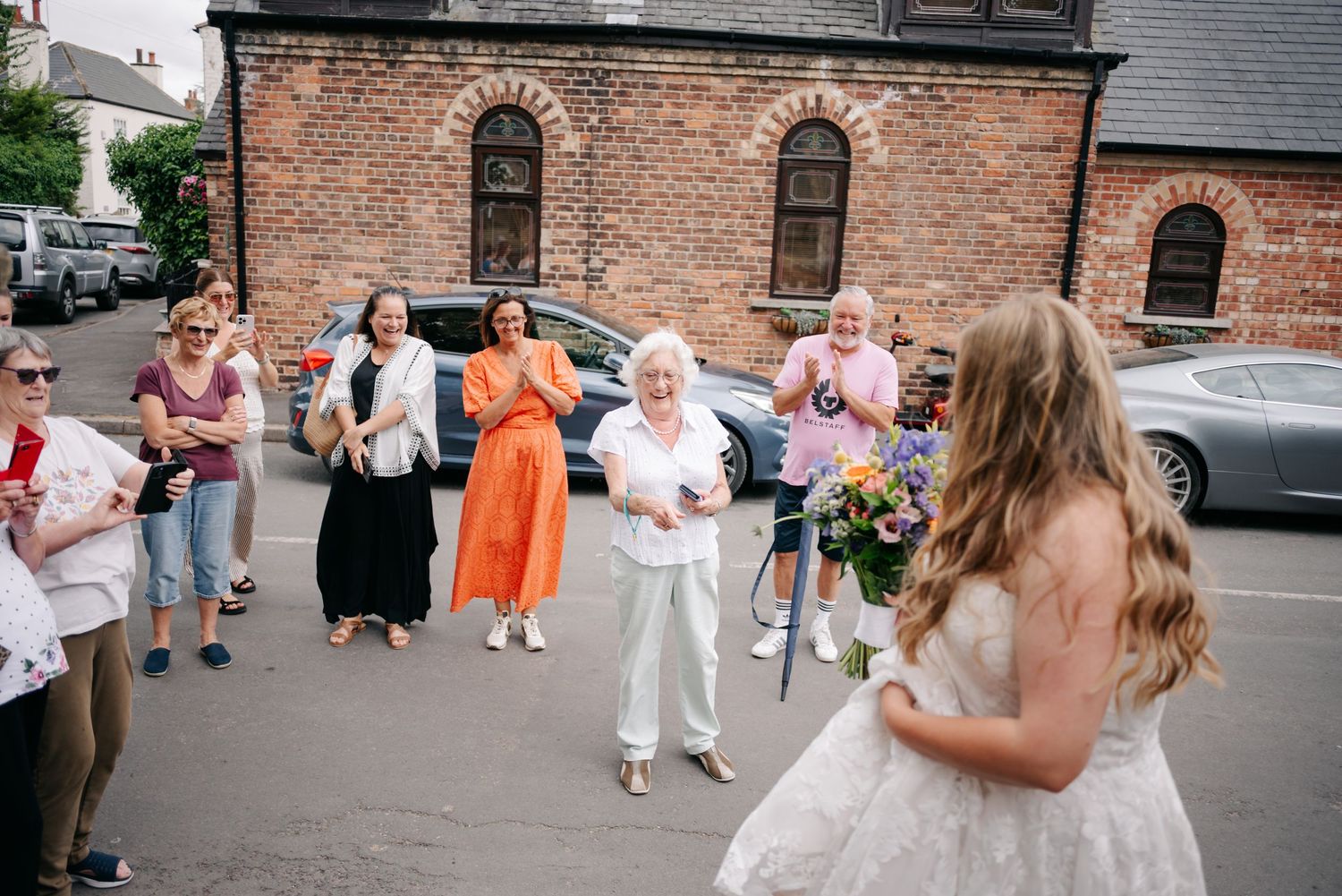 Wedding party dancing and celebrating outside brick church building.